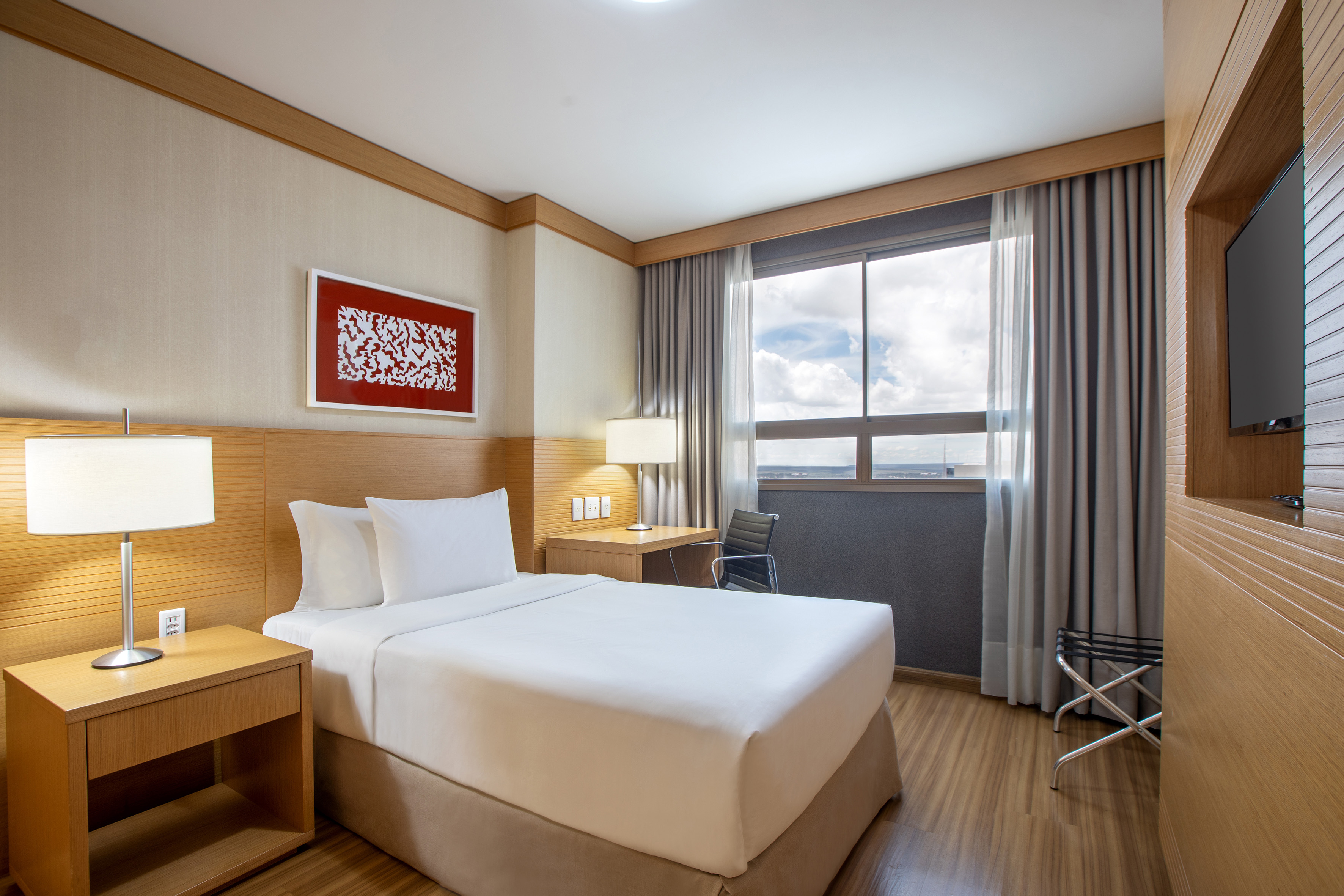 Modern hotel room with single bed, wooden furniture, desk, and window view.