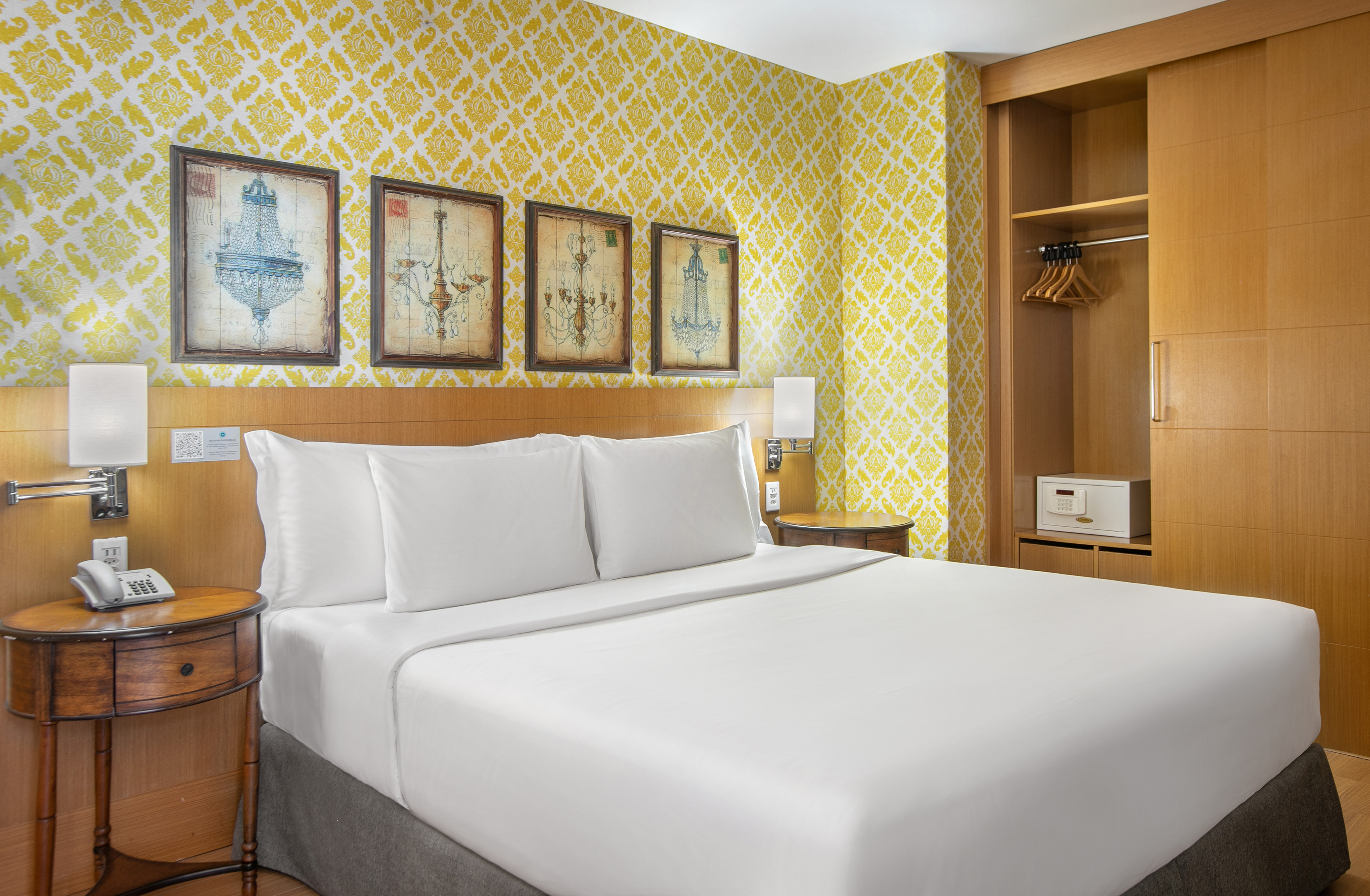 Hotel room, yellow damask wallpaper, white bed, chandelier art, wooden wardrobe.