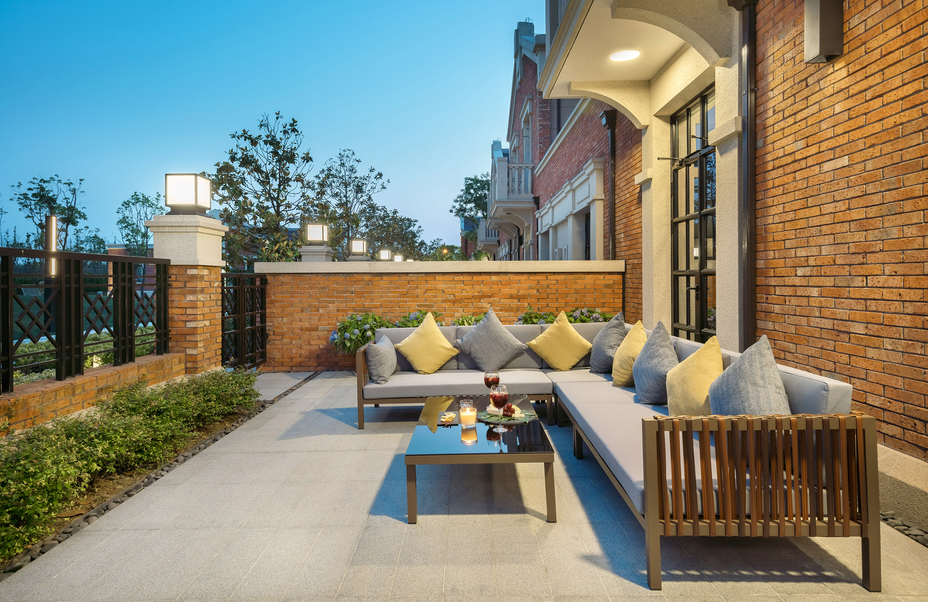 Modern outdoor patio lounge with sectional sofa, glass table, brick house.