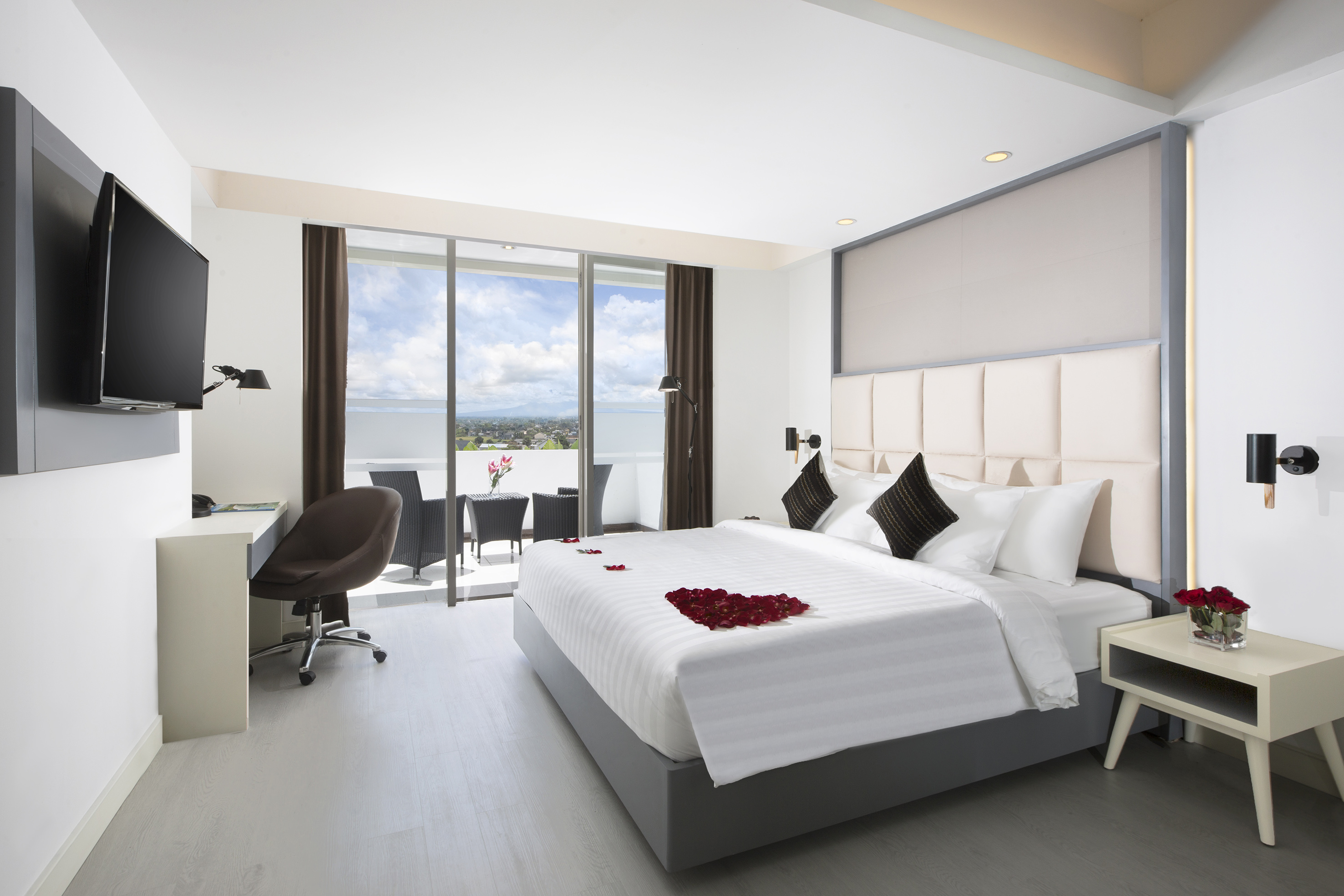 Luxury hotel bedroom with romantic rose petals, balcony and scenic city view.
