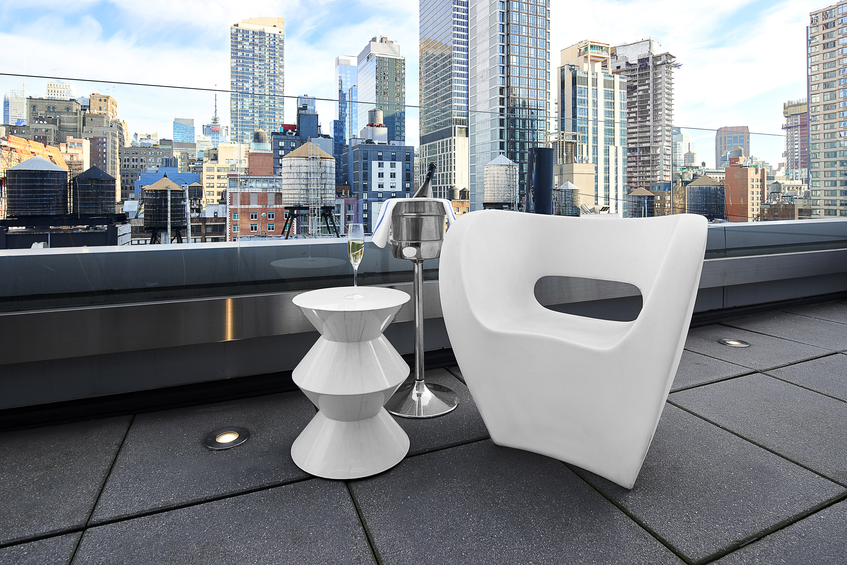 Modern rooftop lounge with white seating, champagne, and urban city skyline.