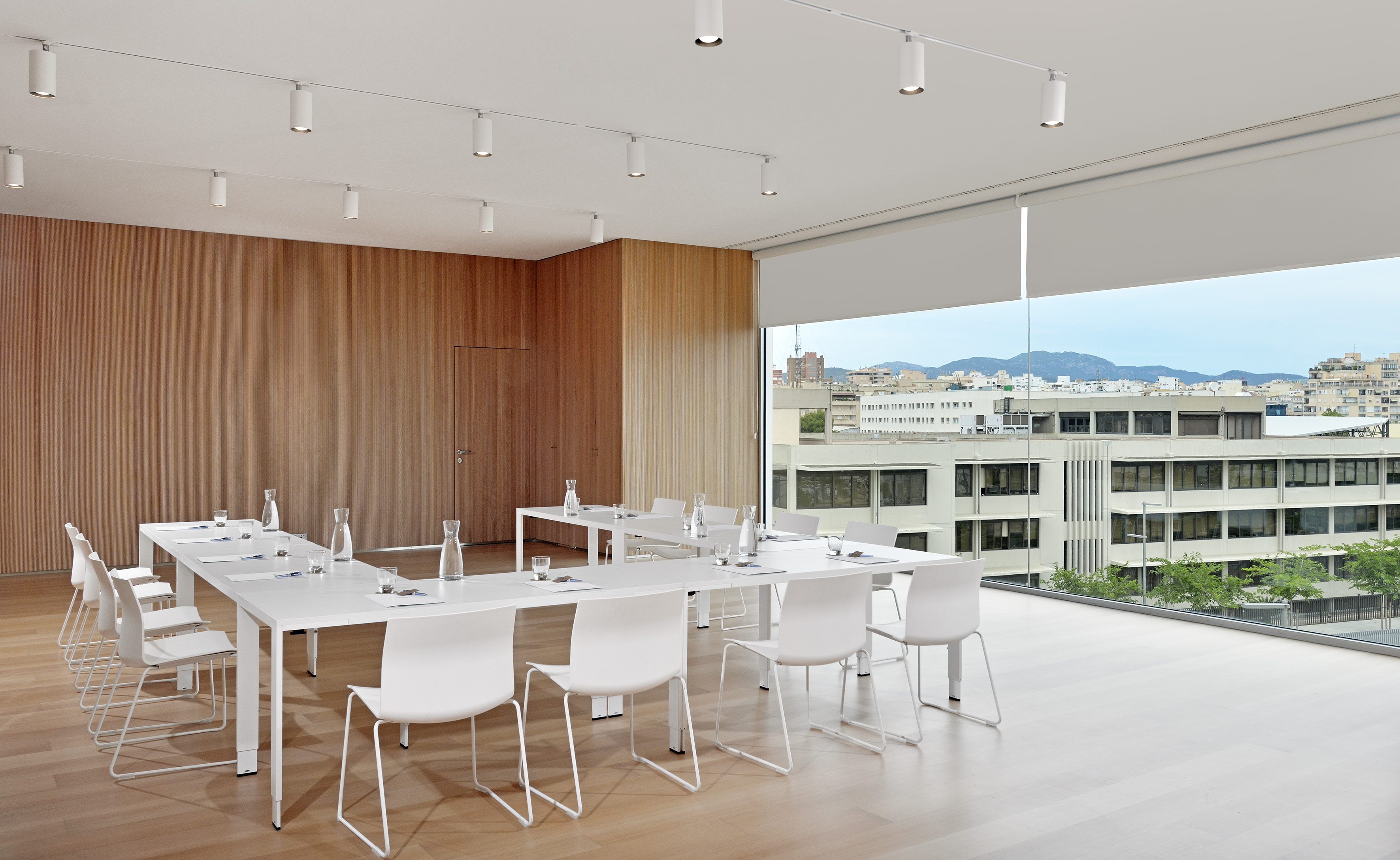 Modern conference room with white tables, chairs, wood paneling, and a city view.
