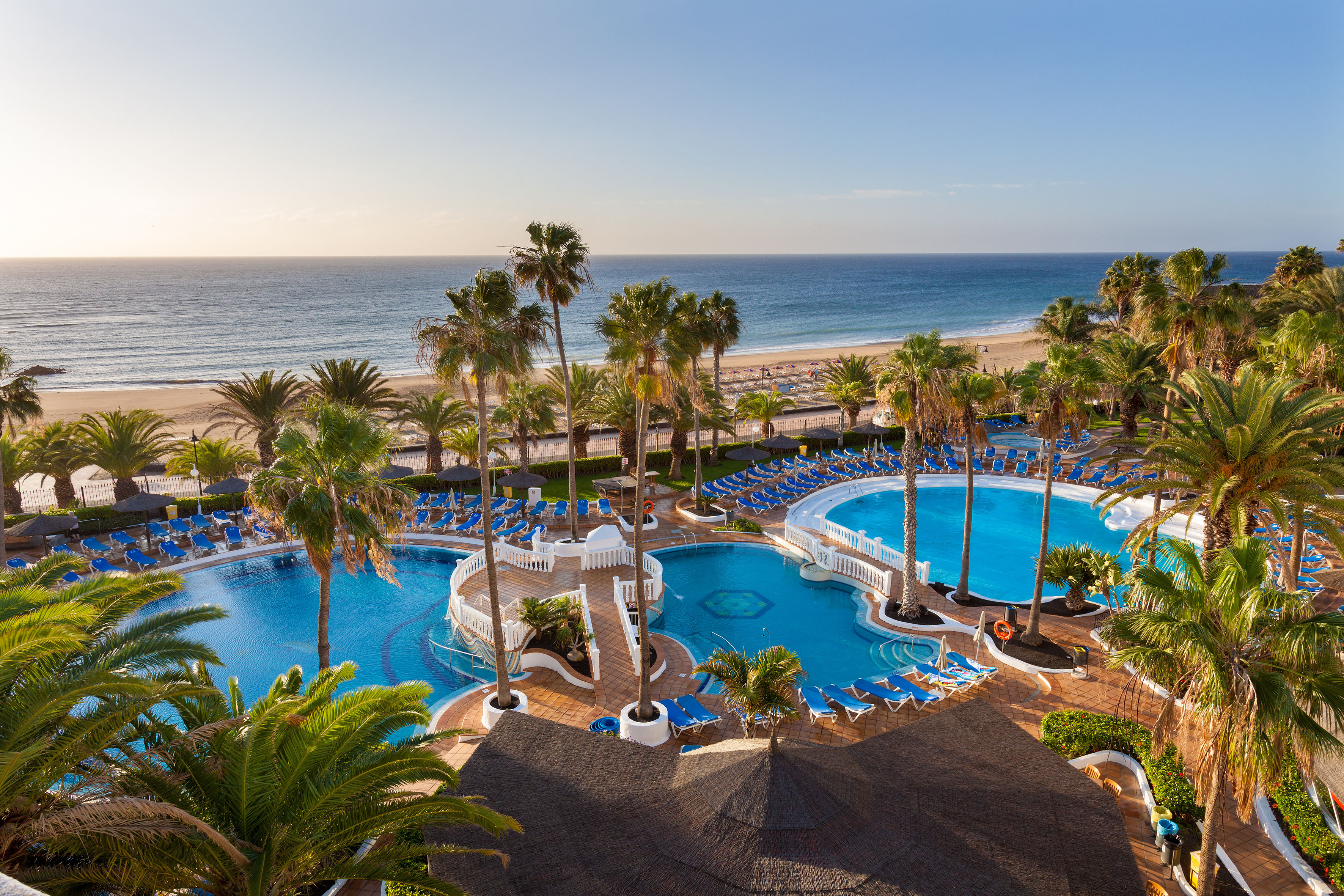 Tropical resort pools, palm trees, sandy beach, and blue ocean.