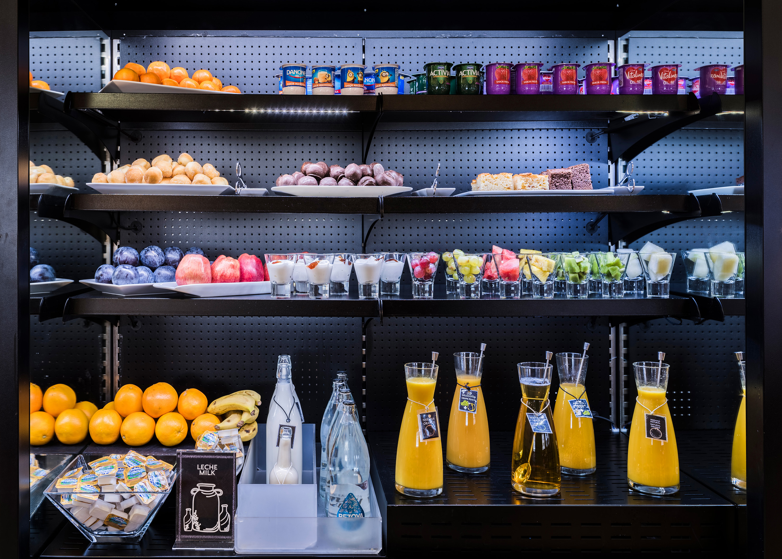 Breakfast buffet featuring fresh fruit, yogurts, juices, pastries, and milk.