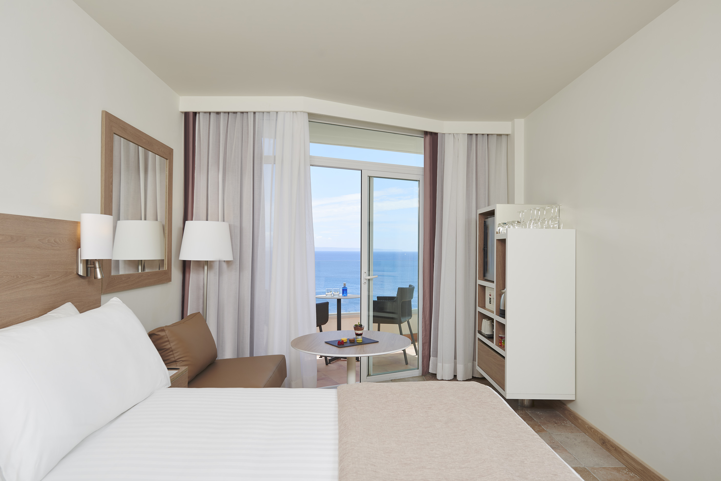 Bright hotel room with sea view balcony, bed, and contemporary furnishings.