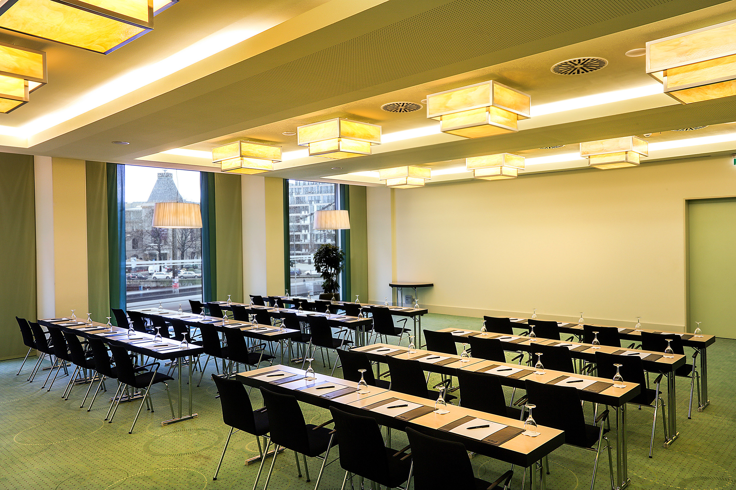 Modern conference room with rows of tables, chairs, green carpet, and bright lighting.