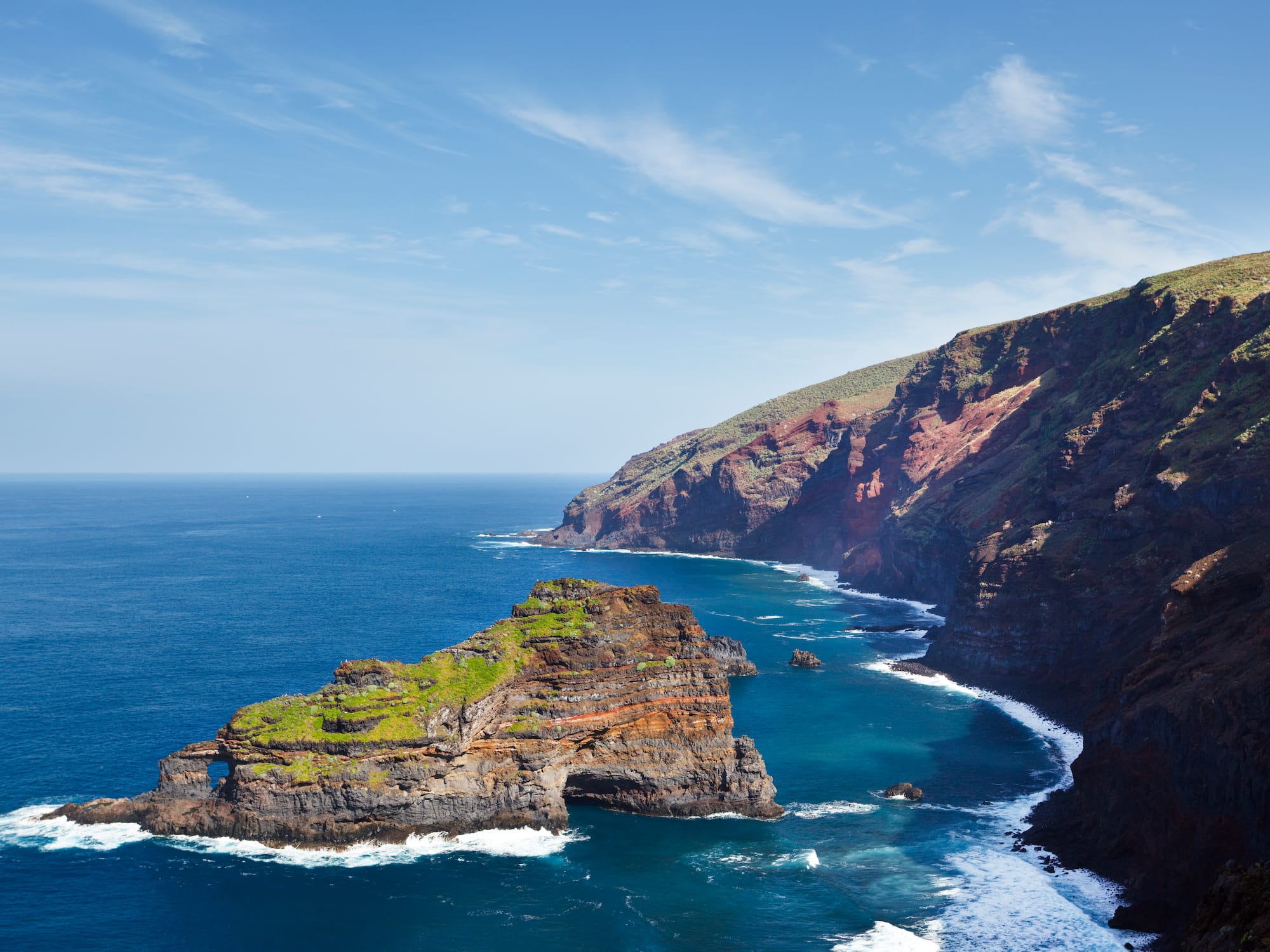 Rugged coastal cliffs and natural sea arch in deep blue ocean waves.
