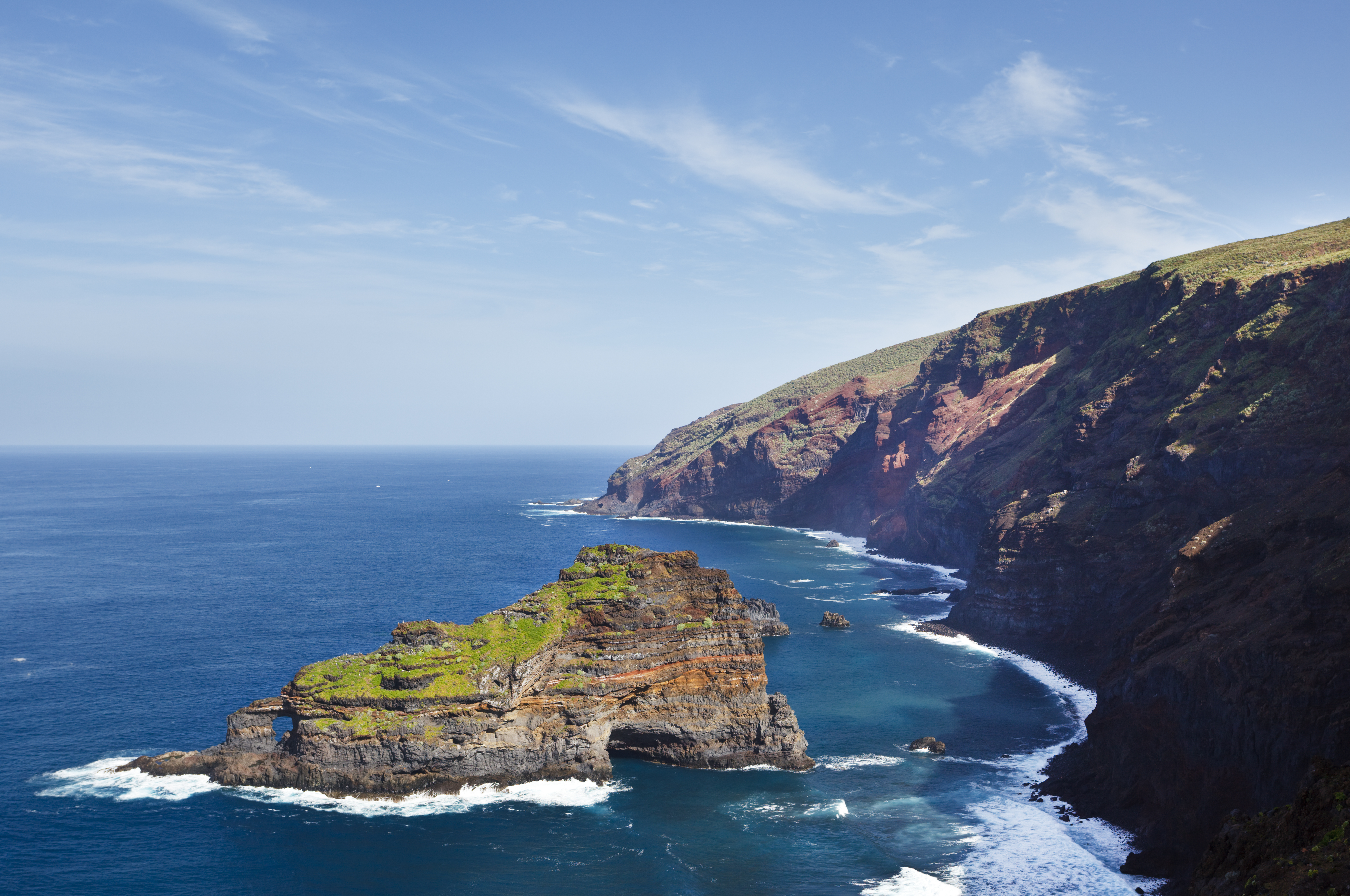 Rugged coastal cliffs and natural sea arch in deep blue ocean waves.