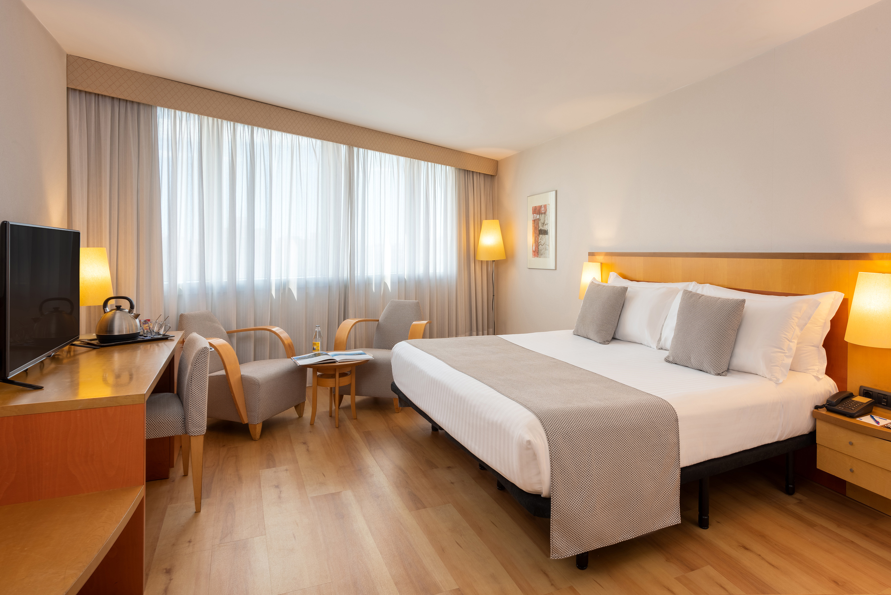 Modern hotel room with king bed, wooden floor, desk, and seating.