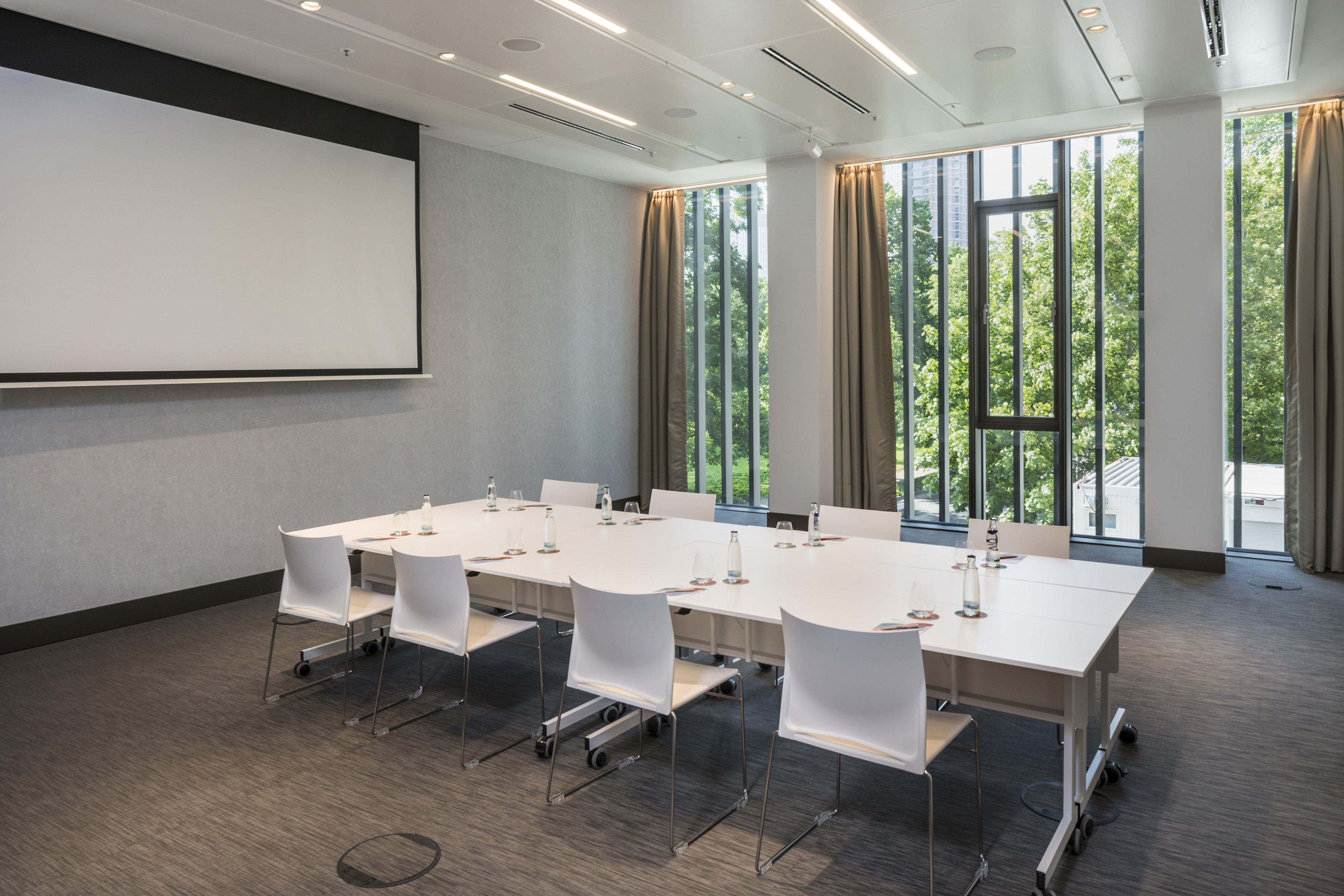 Modern meeting room with projector screen, long table, and large windows.