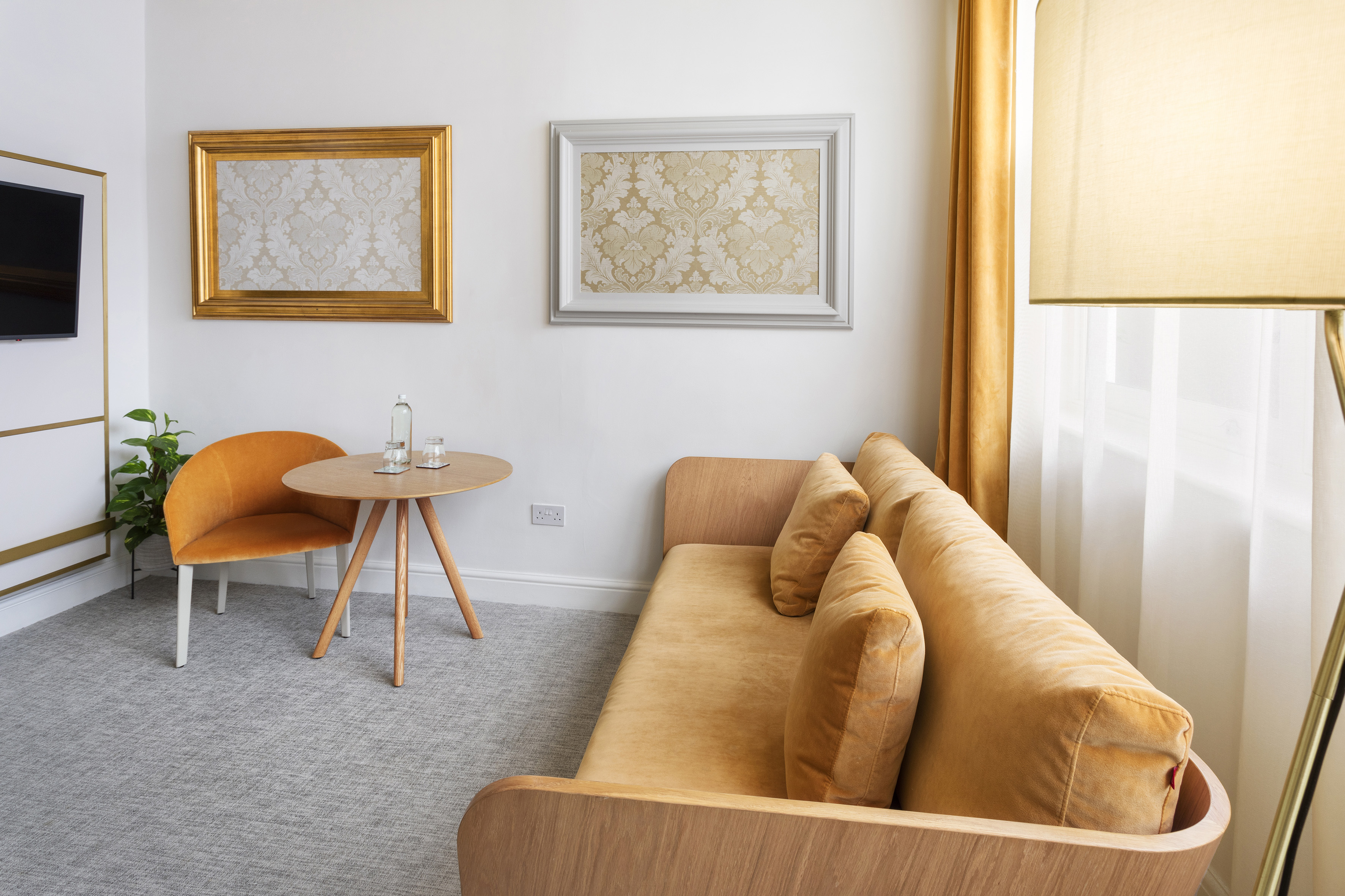 Modern hotel living area with golden sofa, accent chair, and framed art.