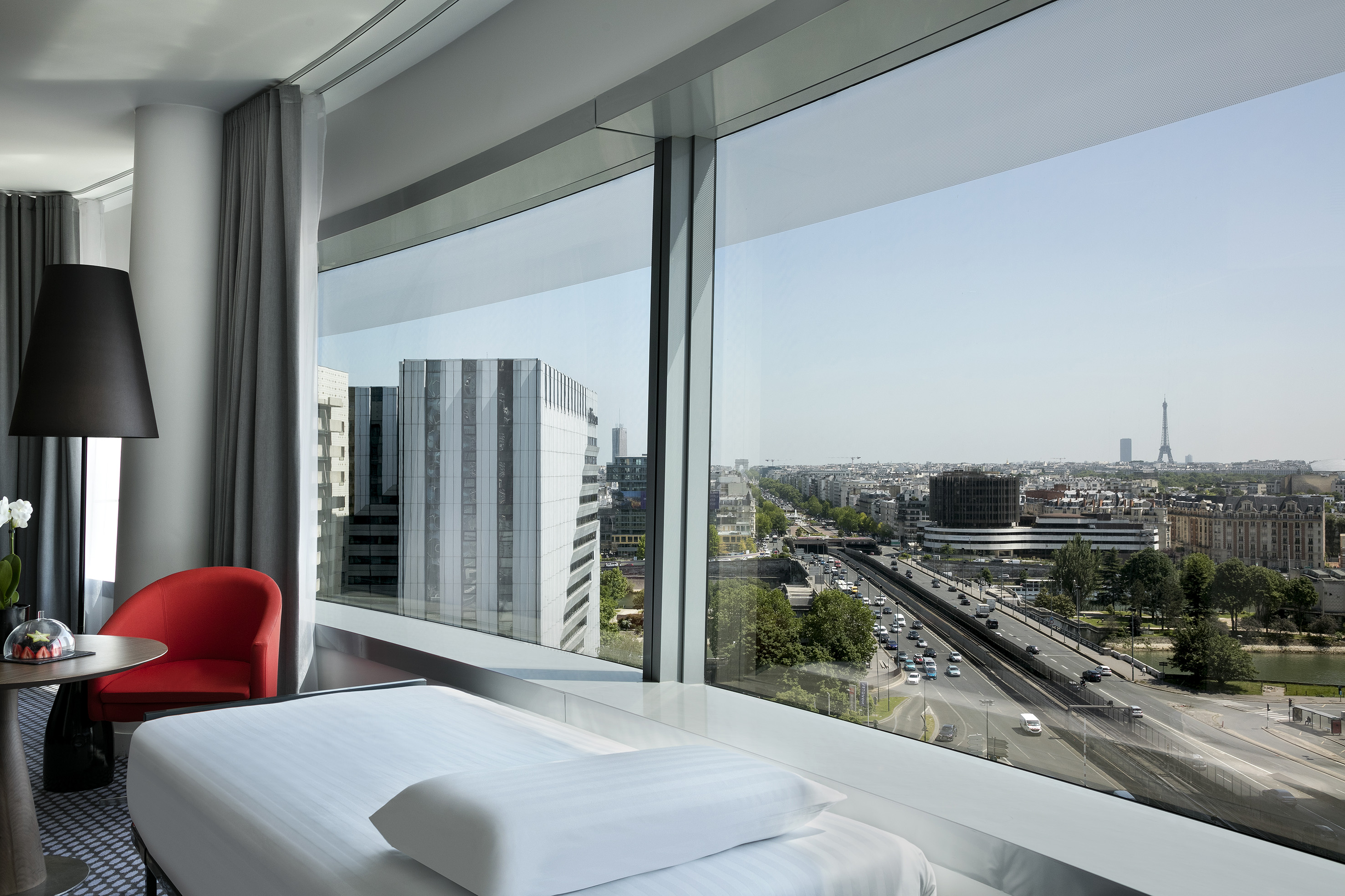 Bedroom with panoramic Paris cityscape, highway, and distant Eiffel Tower.