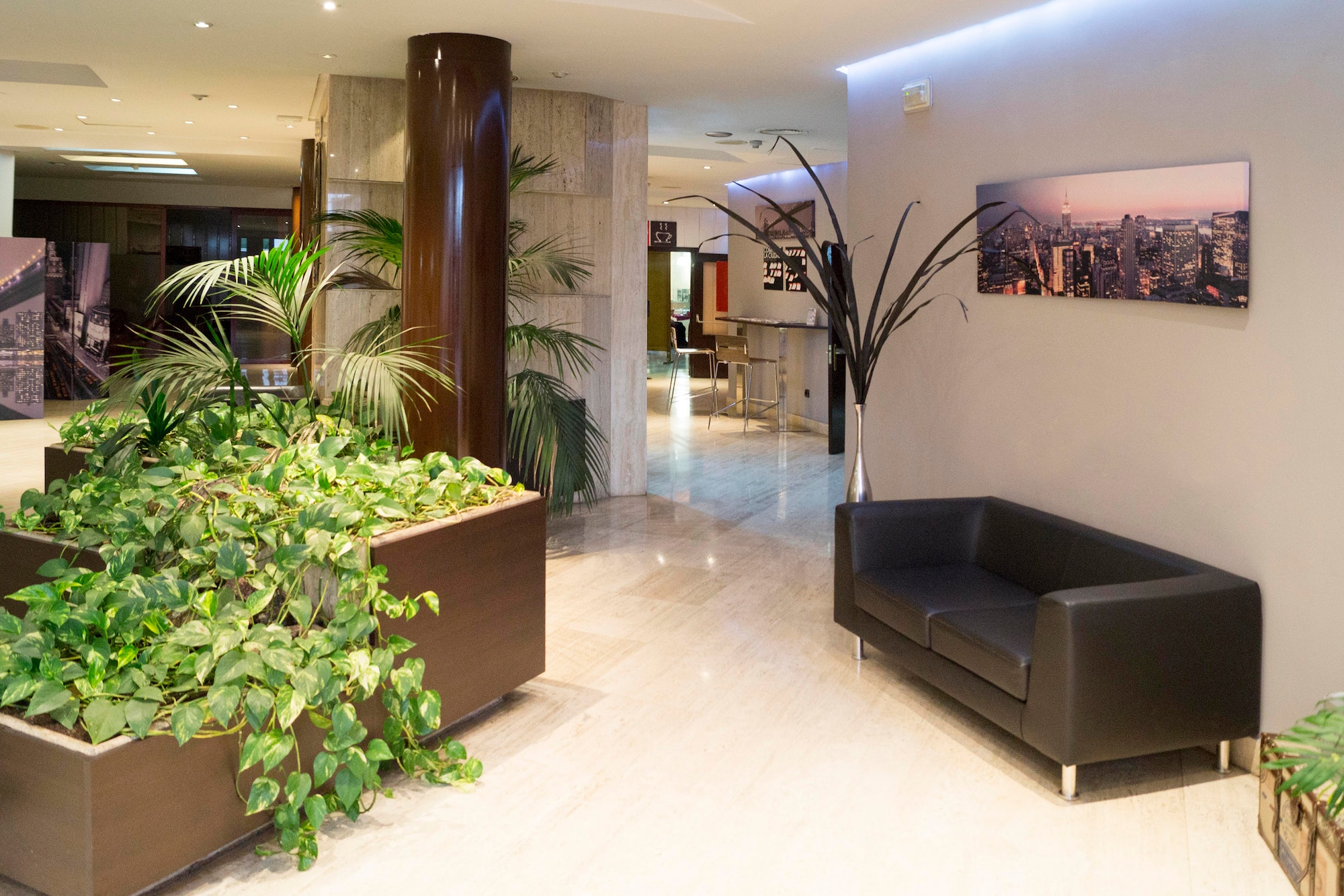 Modern hotel lobby with black sofa, green plants, marble floor, and NYC skyline artwork.