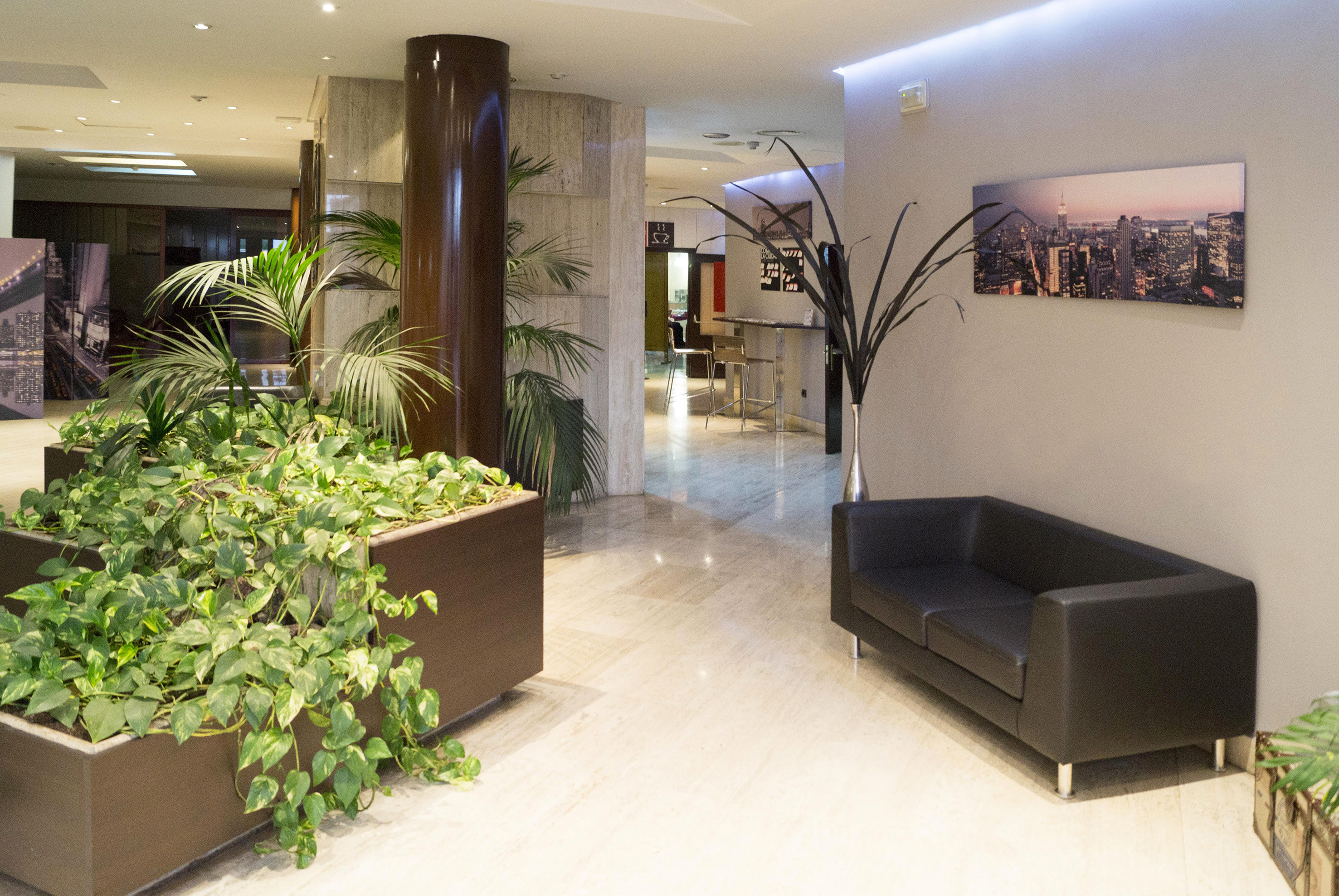 Modern hotel lobby with black sofa, green plants, marble floor, and NYC skyline artwork.