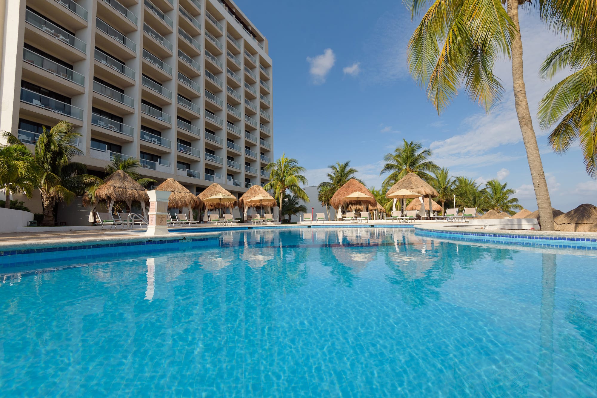 a pool with straw umbrellas and palm trees