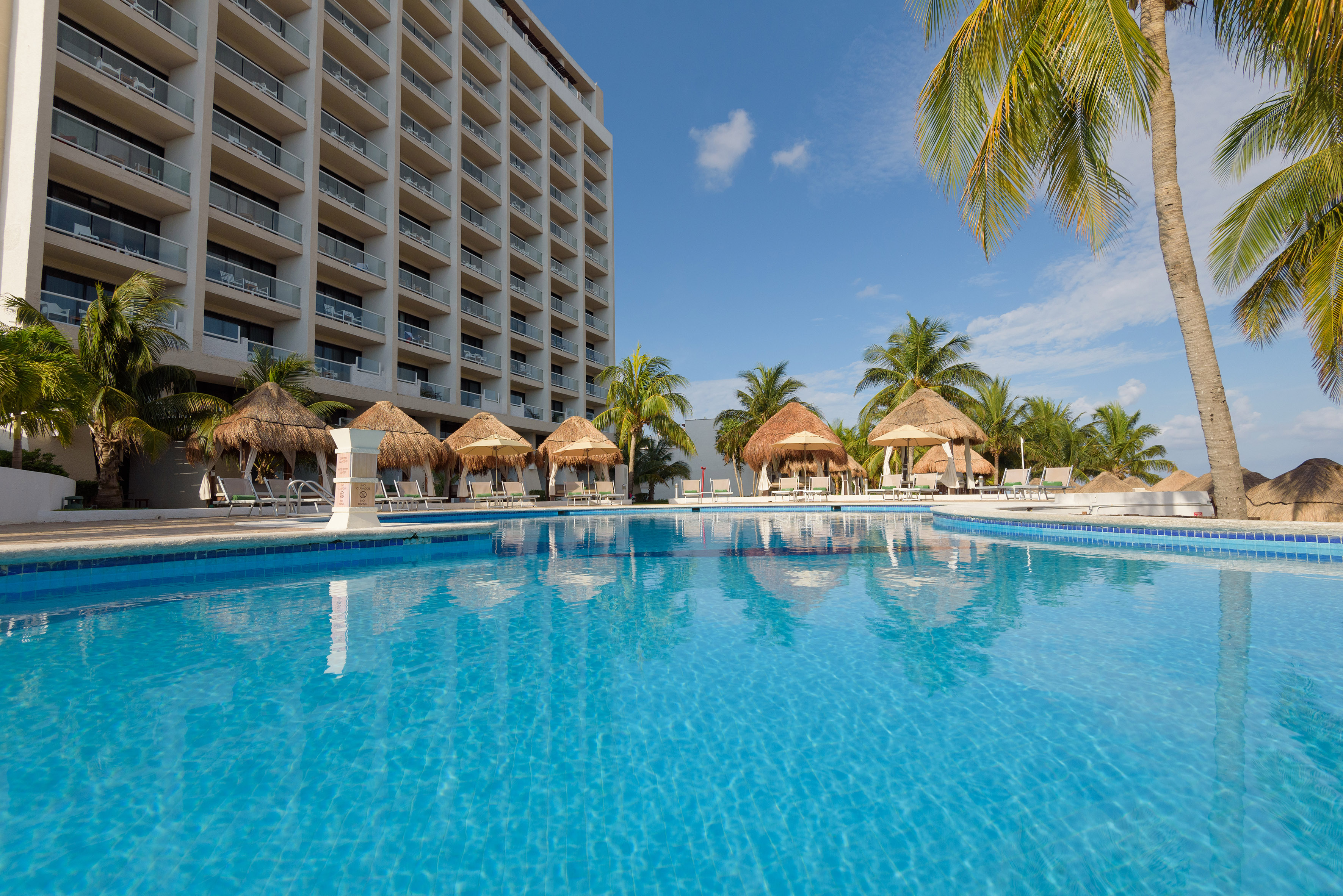 a pool with straw umbrellas and palm trees