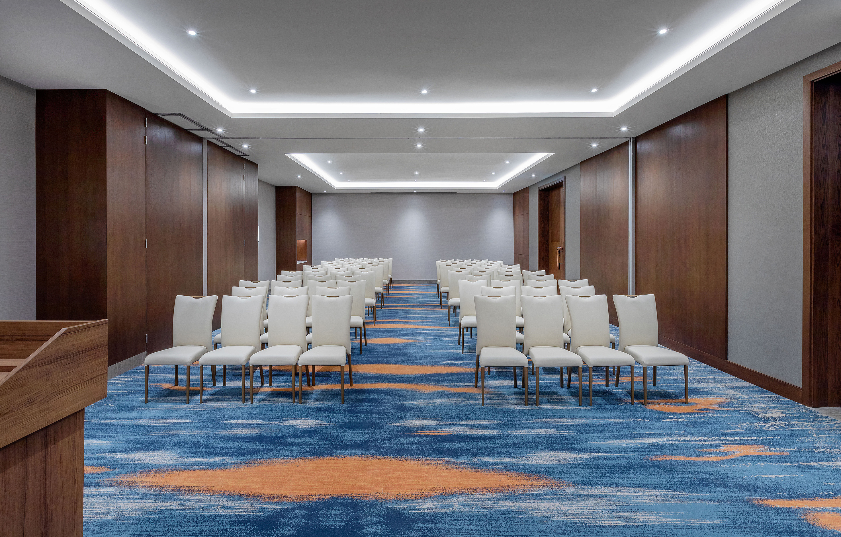 Modern hotel meeting room with white chairs, blue-orange carpet, and wood walls.