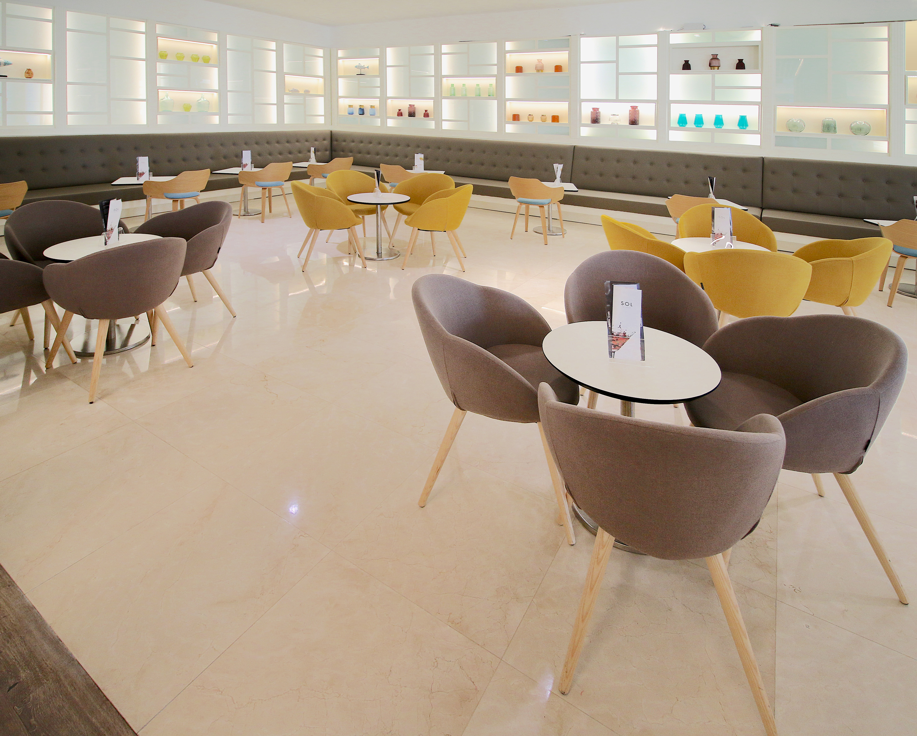 Modern hotel lounge with grey and yellow seating, illuminated display shelves.