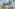 Balcony with rattan furniture, hotel pool, palm trees, and sunny resort view.