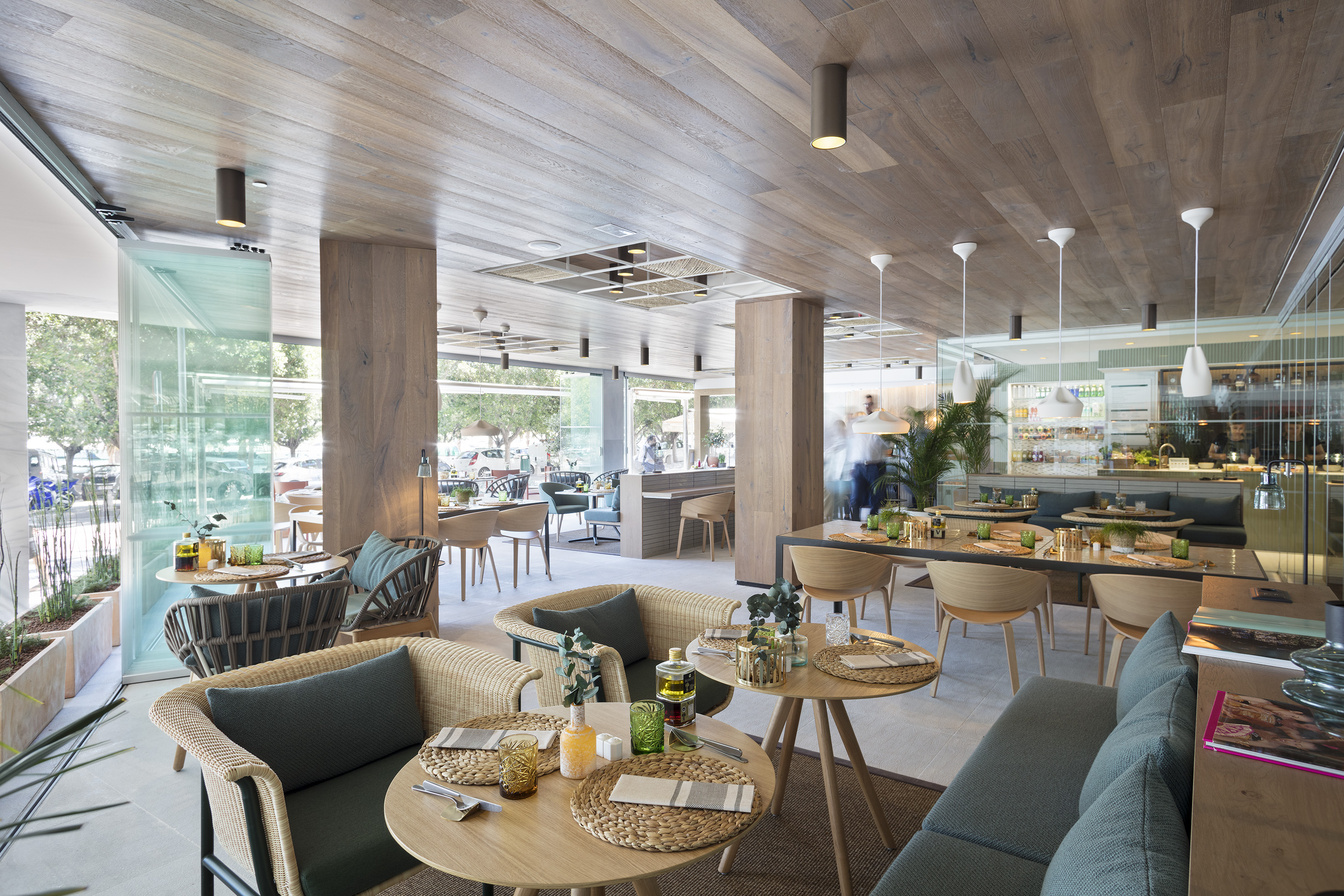 Modern restaurant interior with wood ceiling, wicker chairs, and set tables.