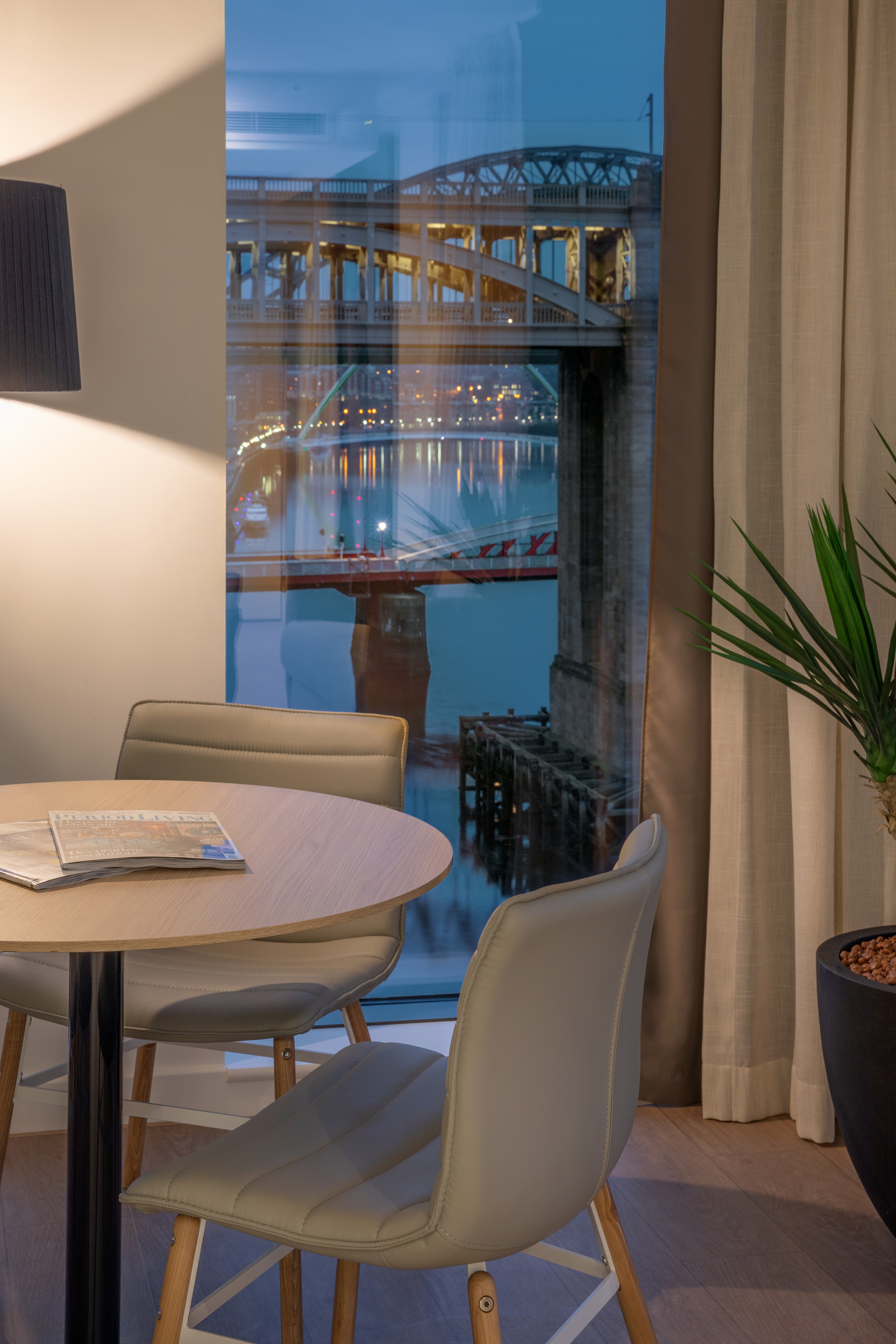 Modern room with table, chairs, and lit Tyne Bridge river view at night.