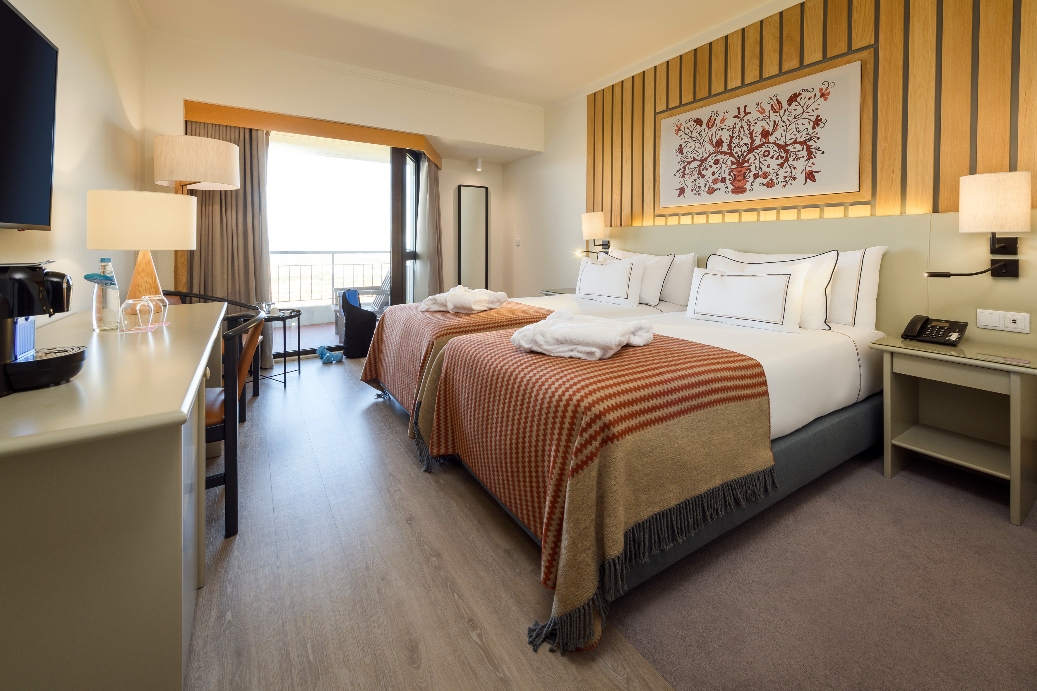 Modern hotel room with twin beds, bathrobes, balcony, and wood accents.