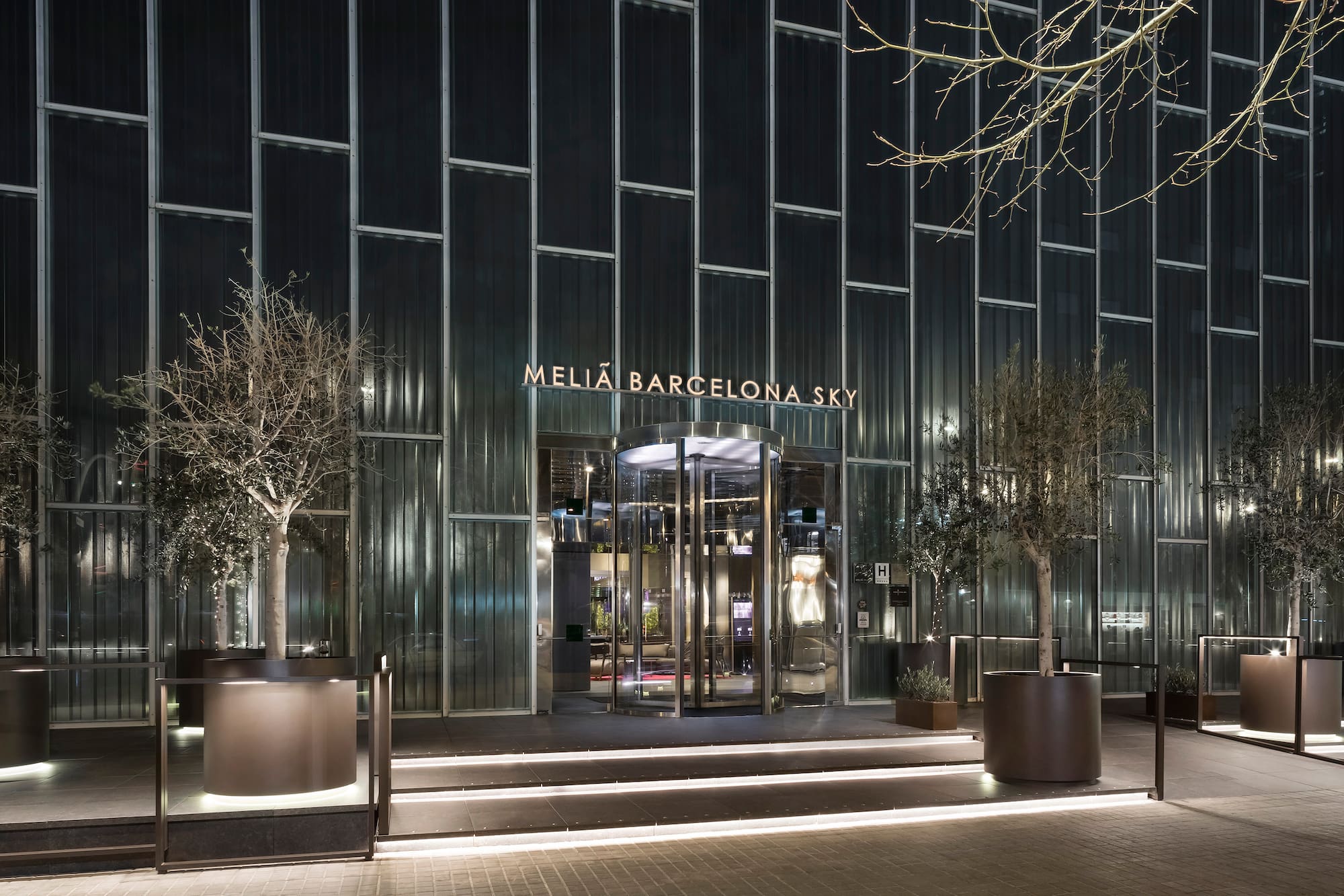 Meliá Barcelona Sky hotel entrance at night, illuminated sign, modern glass facade.
