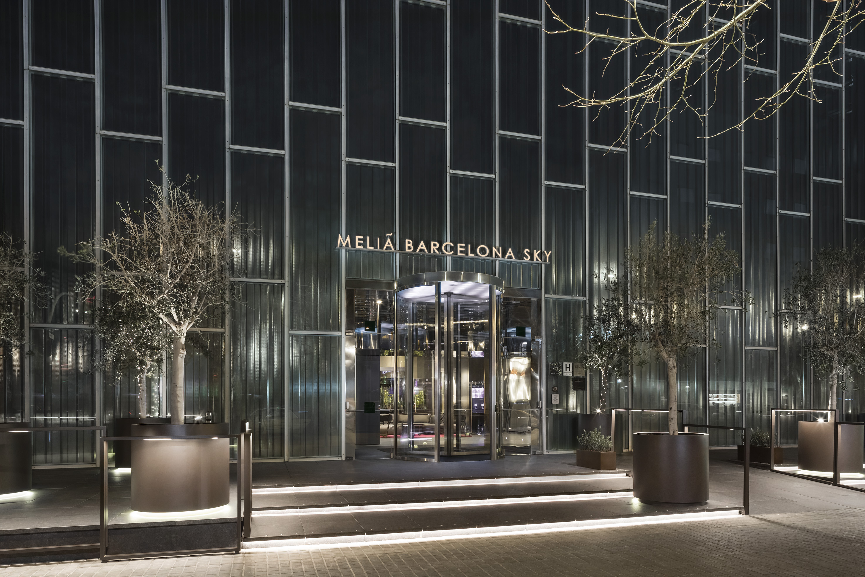 Meliá Barcelona Sky hotel entrance at night, illuminated sign, modern glass facade.