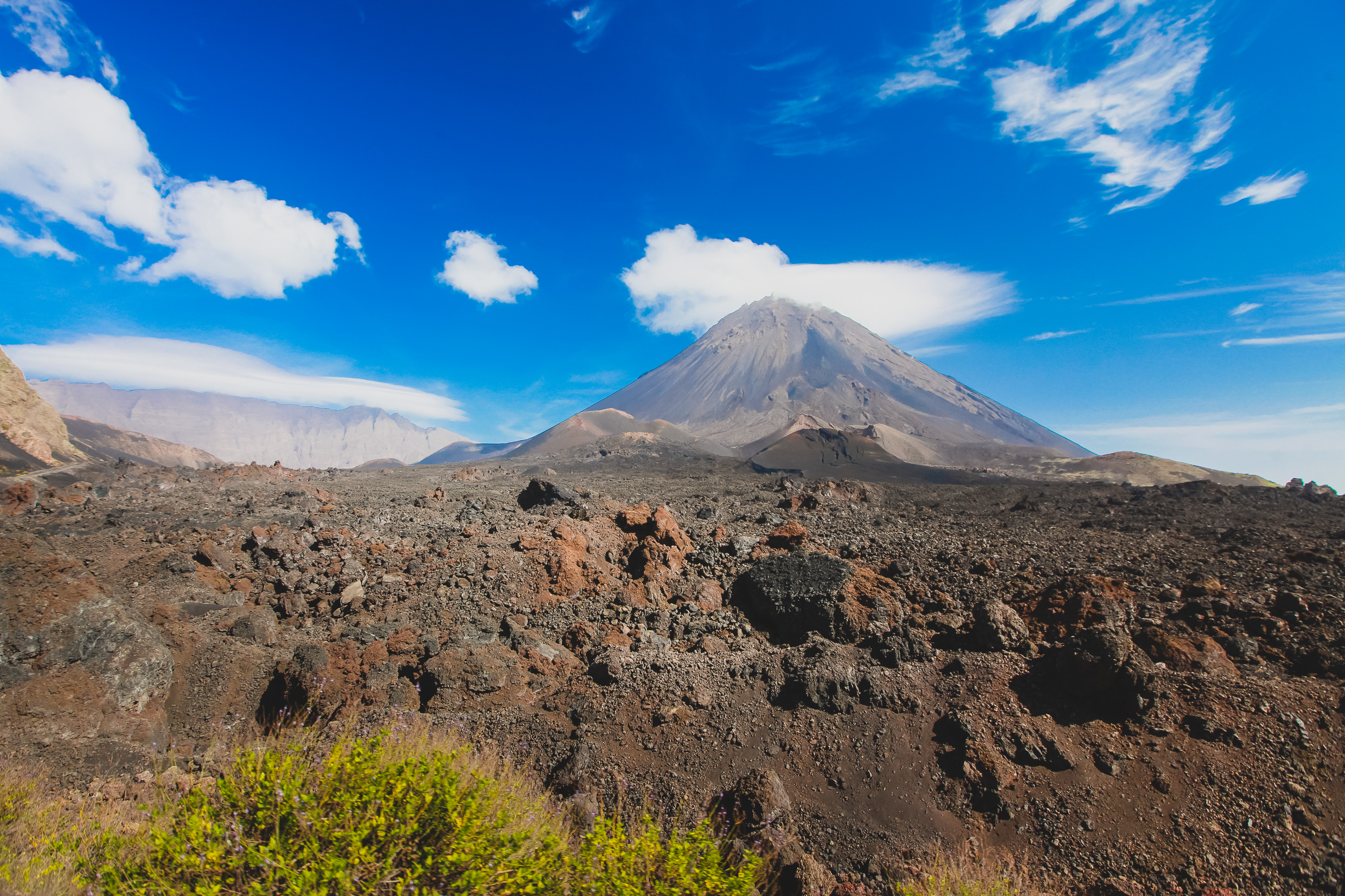 Paisaje volcánico de Fogo con volcán cónico, rocas y cielo azul.