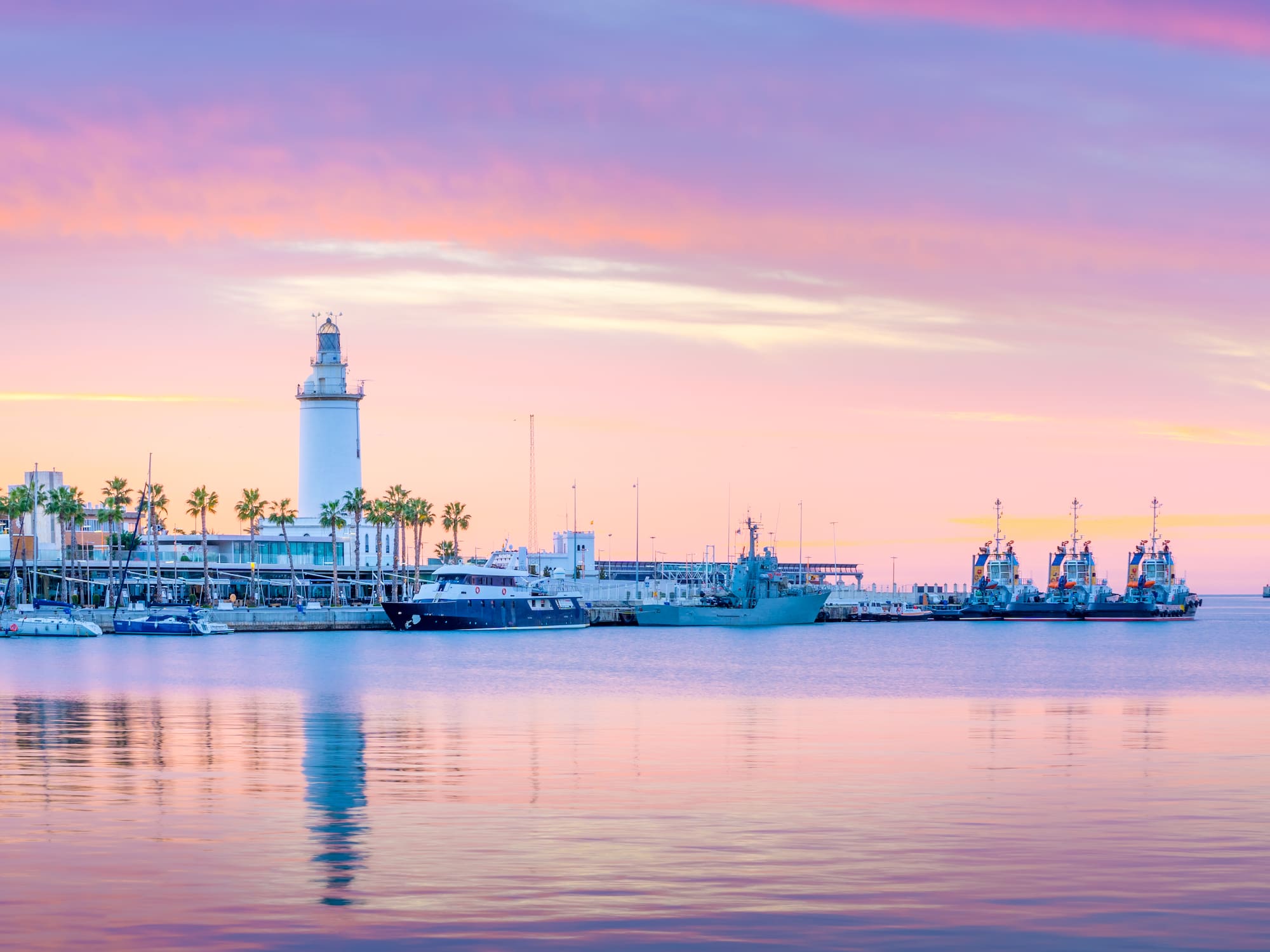 Vibrant pink and purple sunset over Malaga port with lighthouse, boats, and palms.