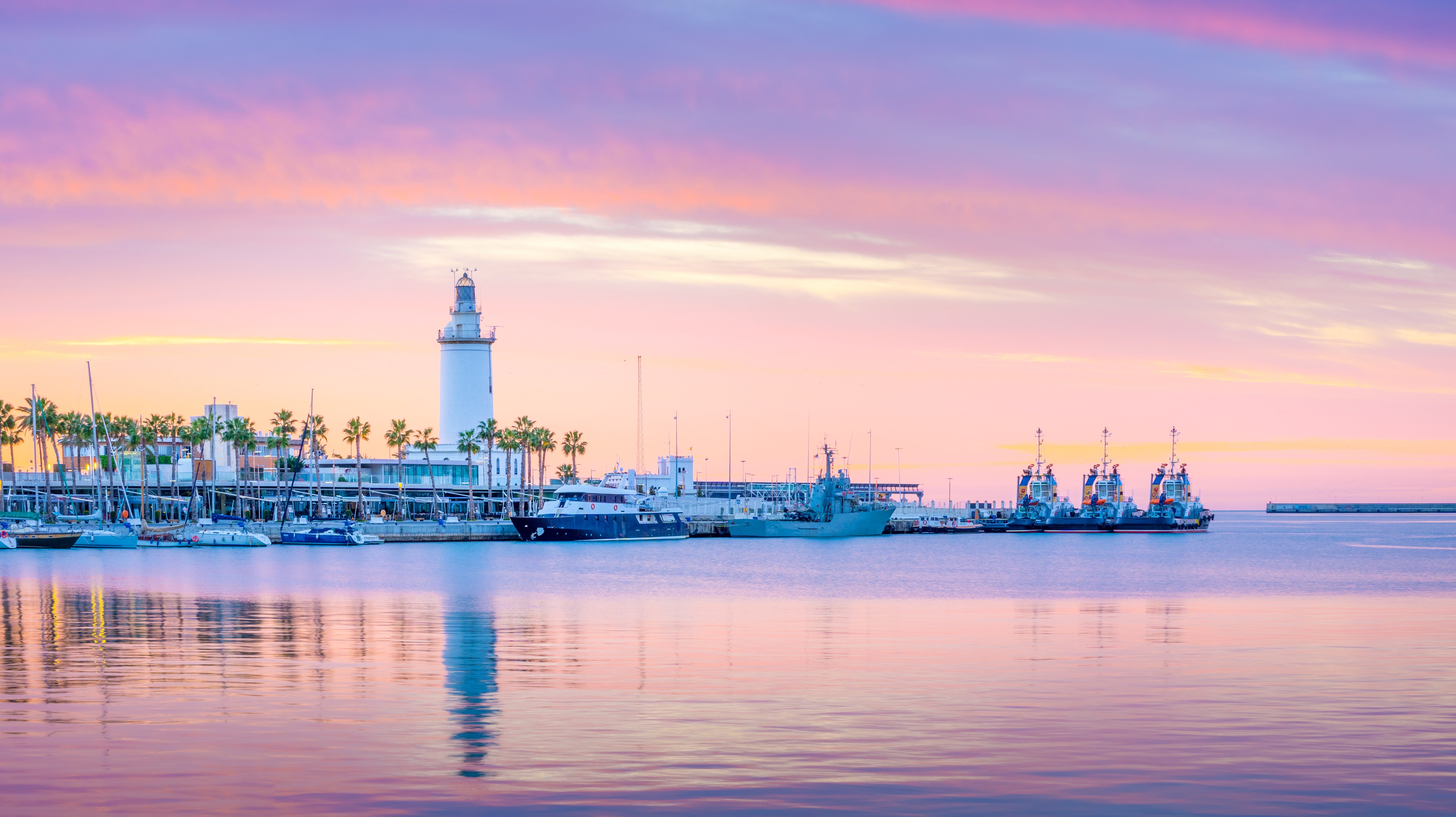 Vibrant pink and purple sunset over Malaga port with lighthouse, boats, and palms.