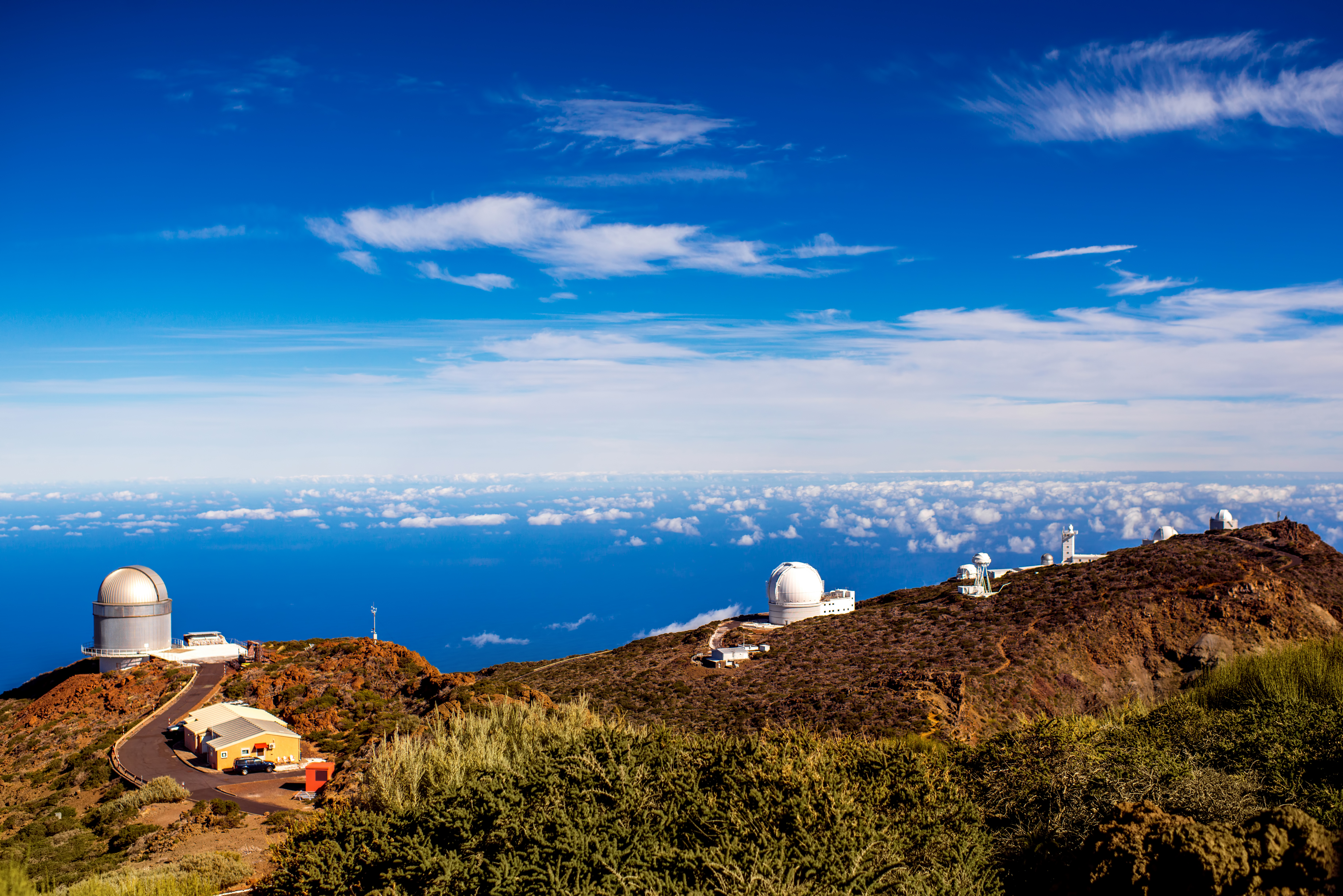 Mountain observatory with white domes, sea of clouds, and deep blue sky.