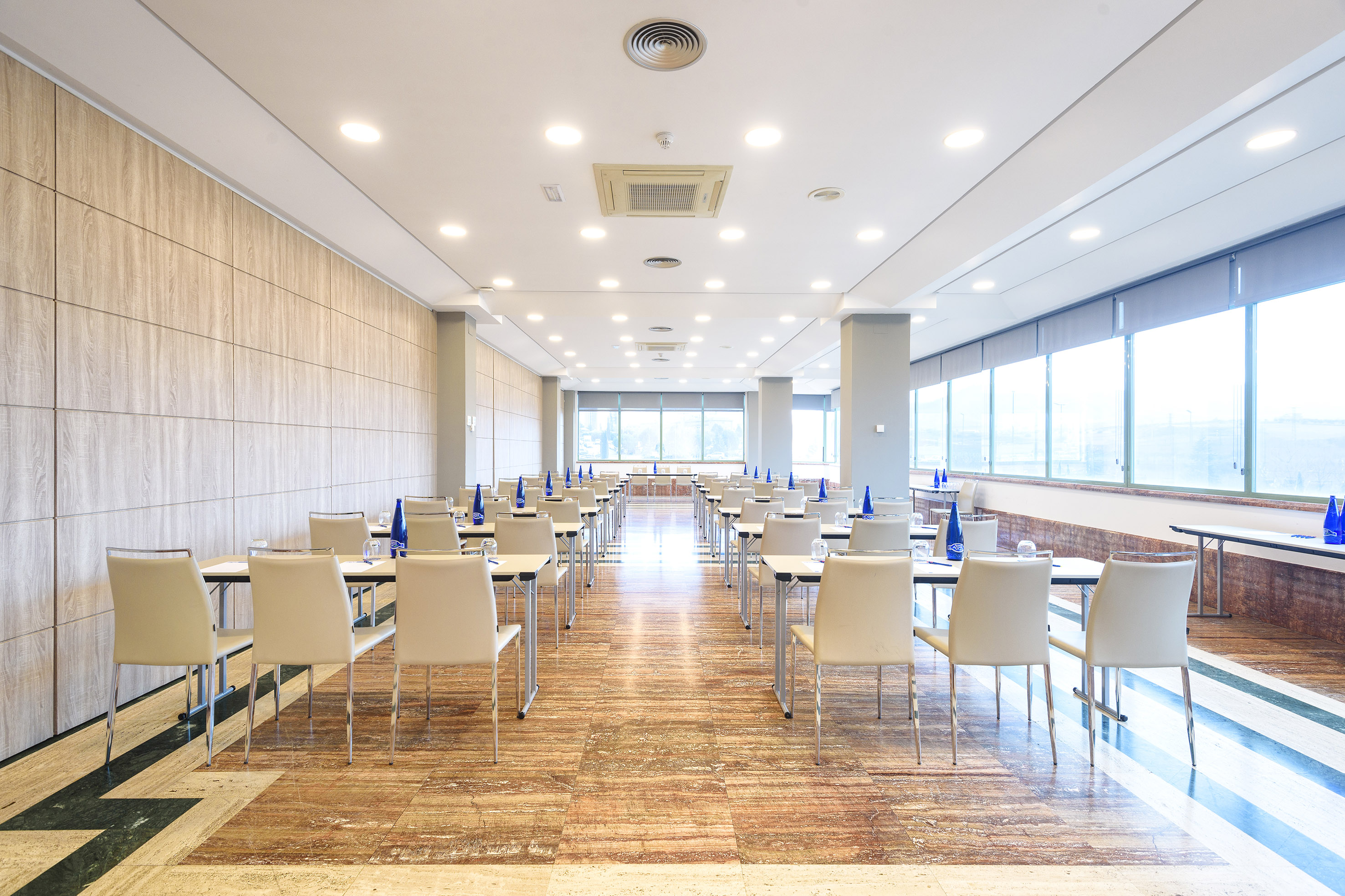 Modern conference room with rows of tables, cream chairs, and large windows.