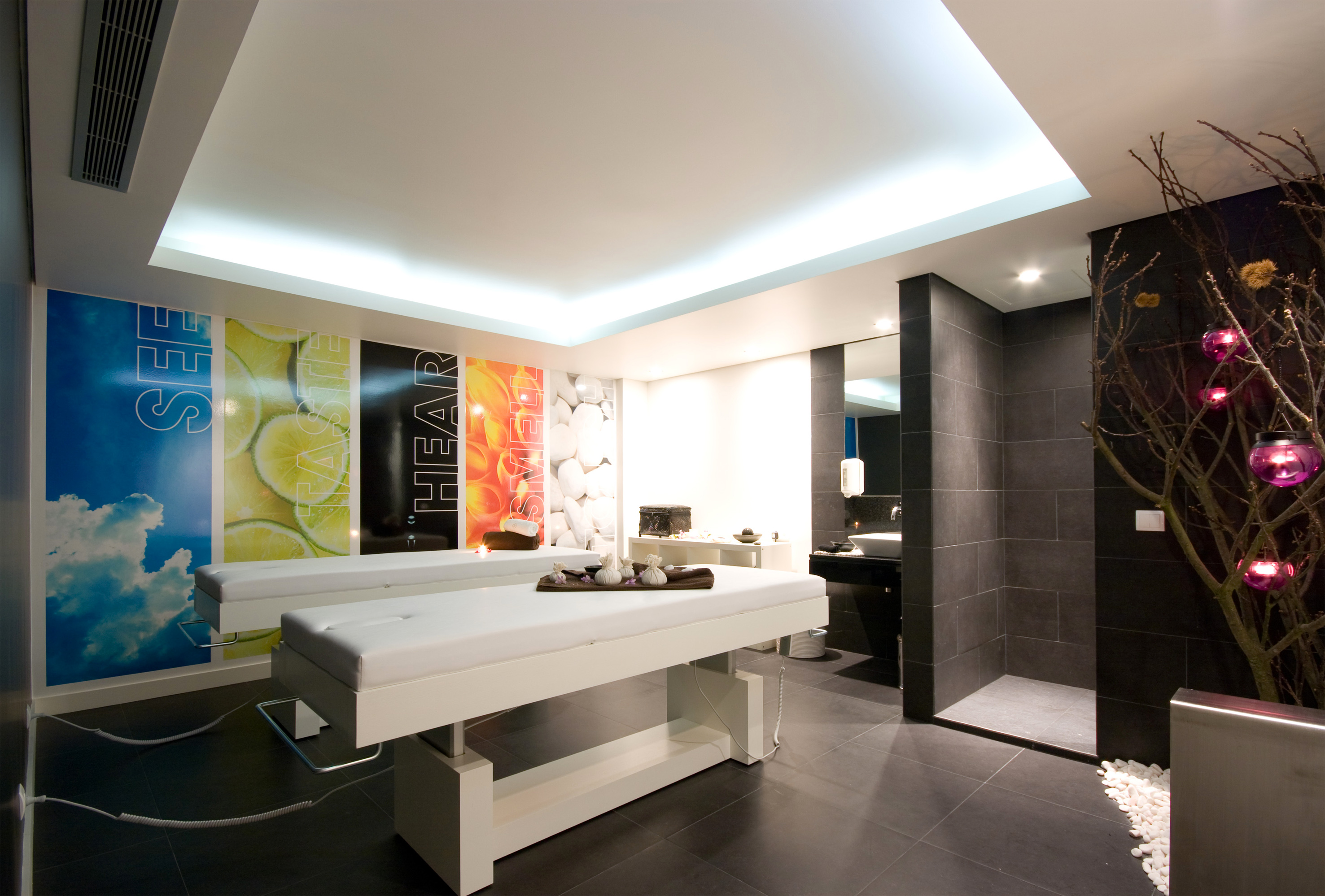 Modern spa treatment room with two massage beds and sensory wall art.