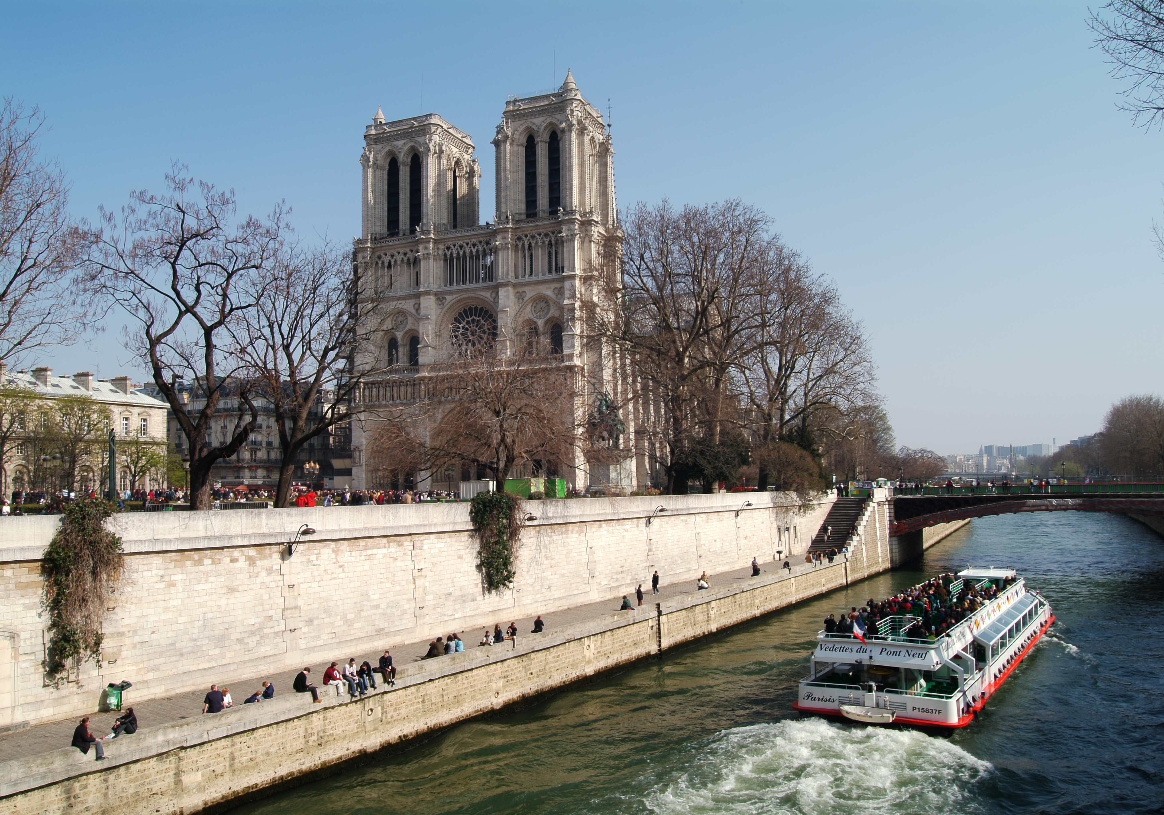 Notre Dame Cathedral and Seine River cruise boat in Paris with people on banks.
