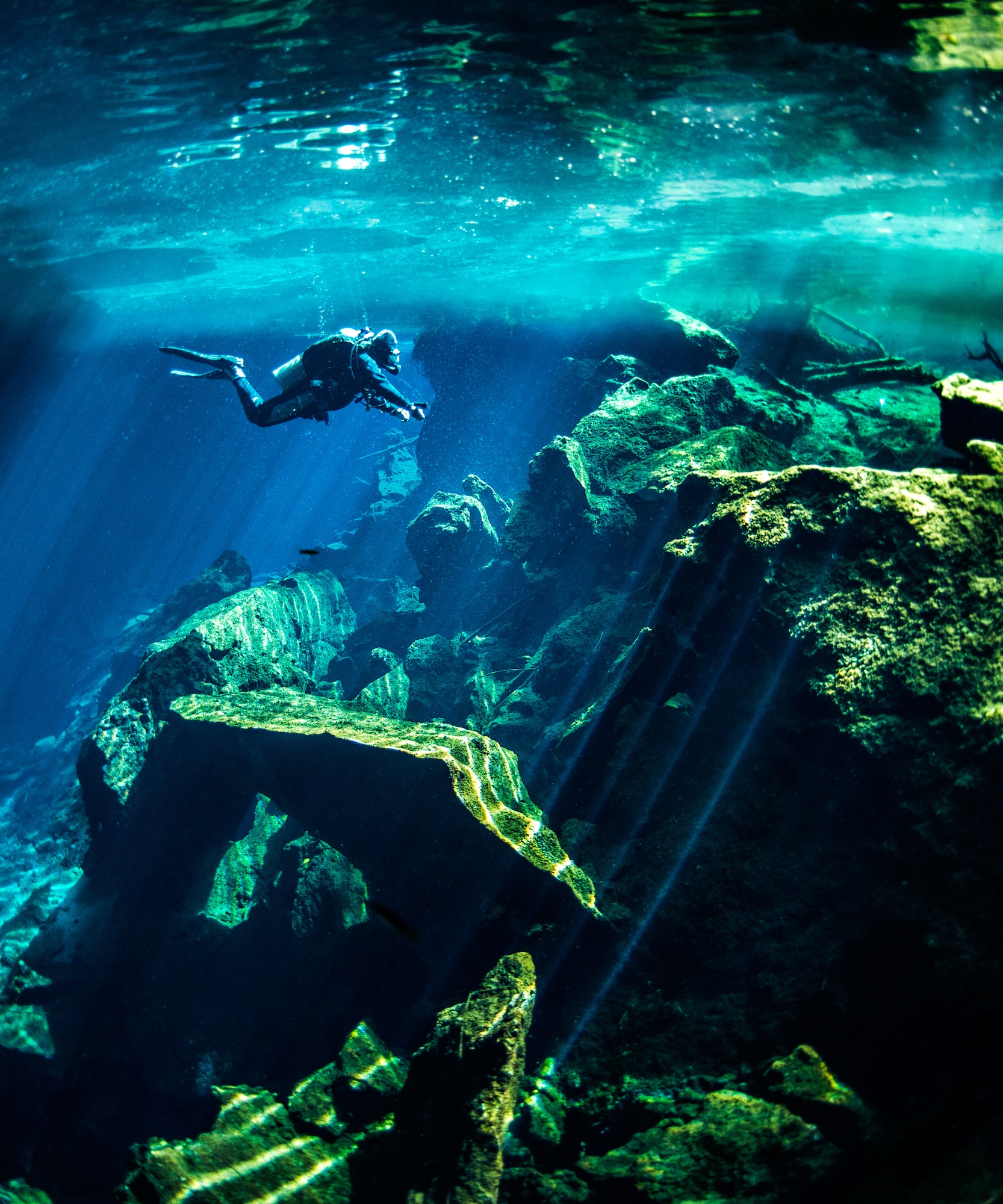 Buceador explorando cenote con rayos de sol entre rocas.
