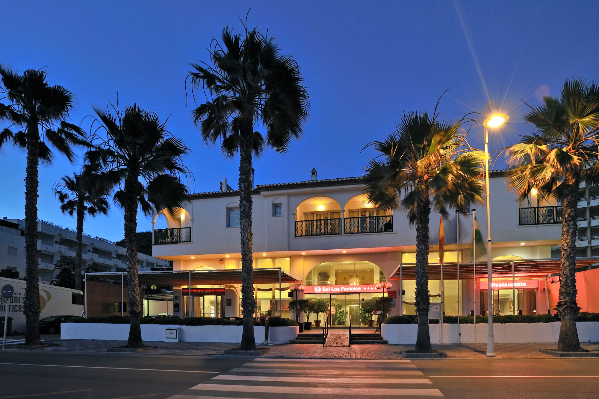 Illuminated Sol Los Fenicios hotel facade with palm trees at dusk.