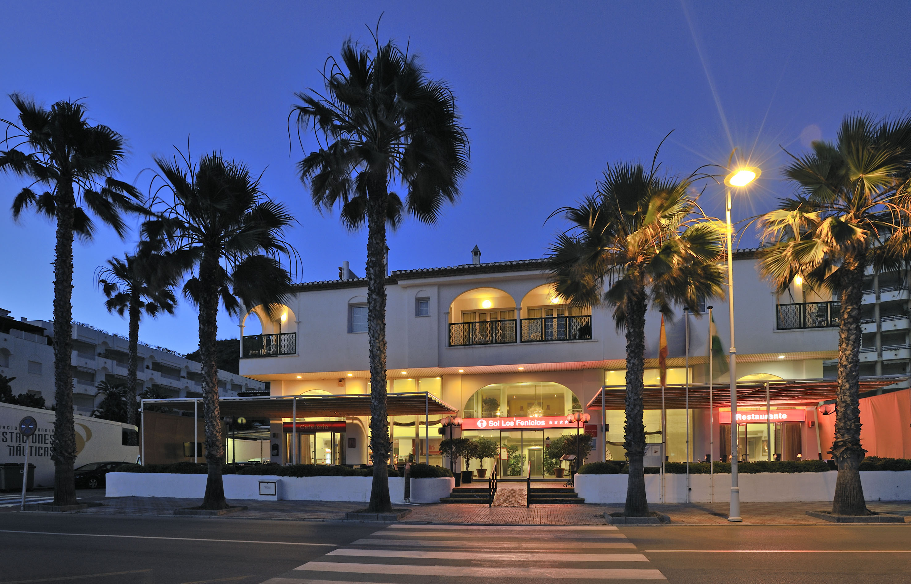 Illuminated Sol Los Fenicios hotel facade with palm trees at dusk.