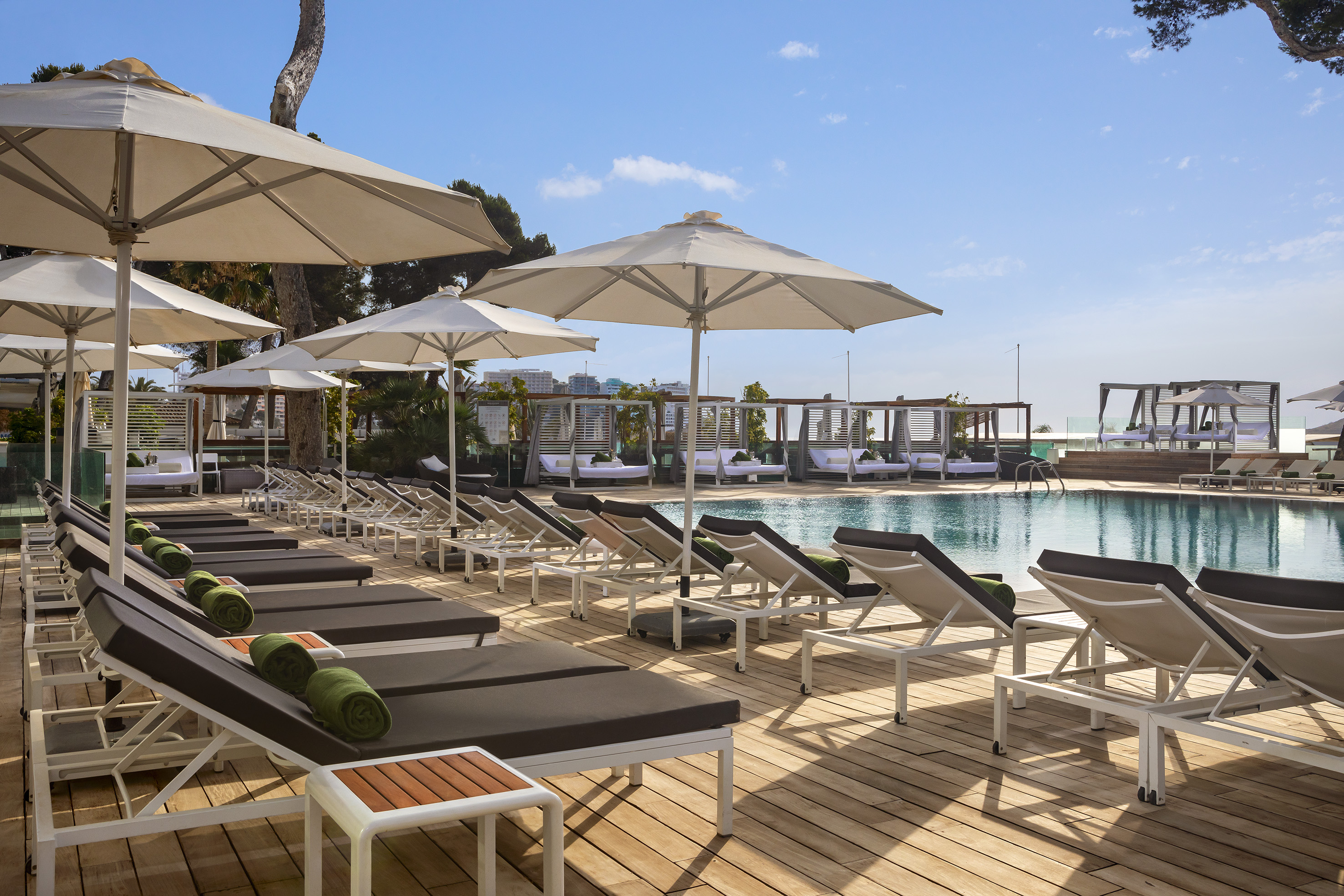 Sunny resort pool deck with sun loungers, umbrellas, and cabanas.
