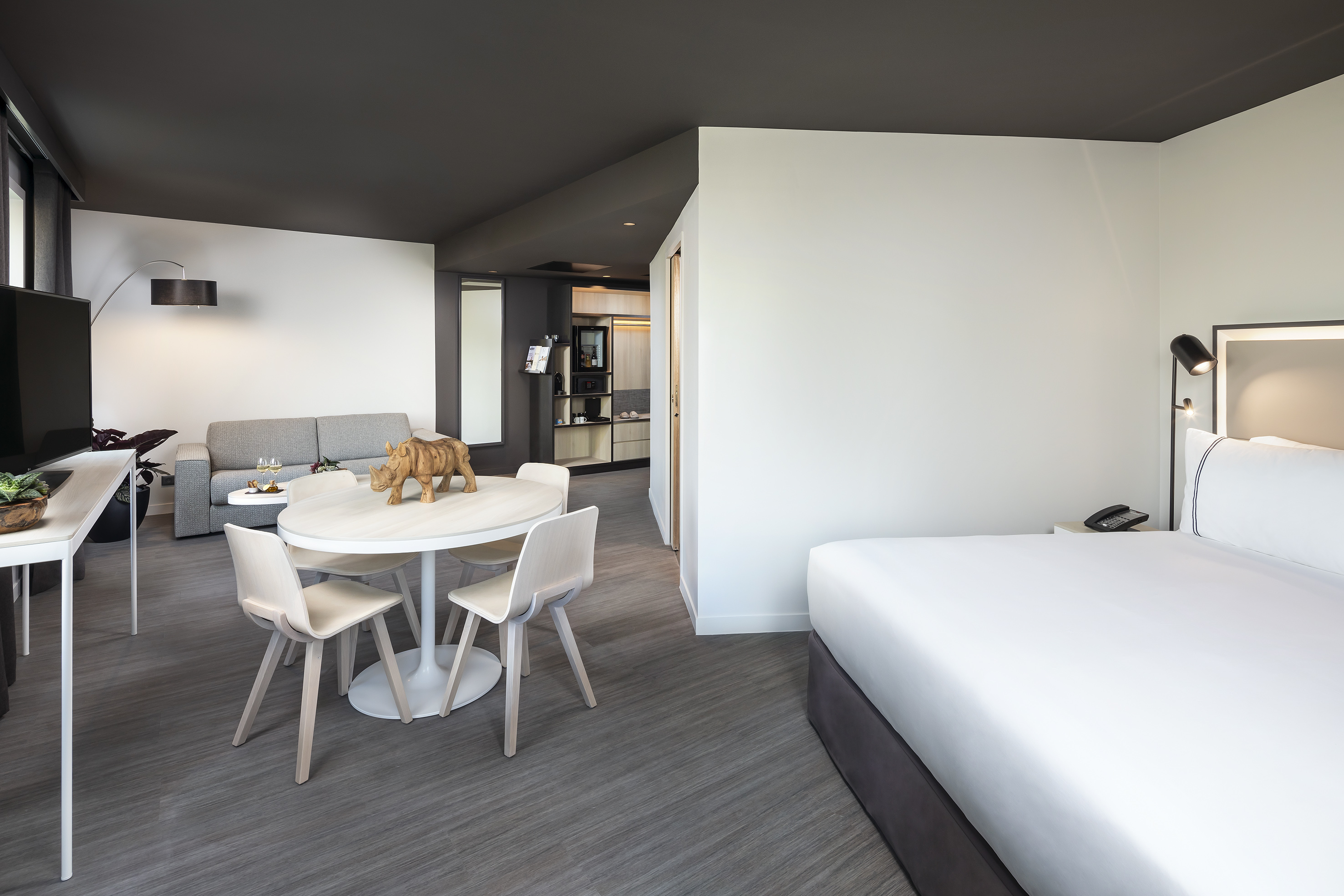 Modern hotel suite with bed, dining table, sofa, and kitchenette.
