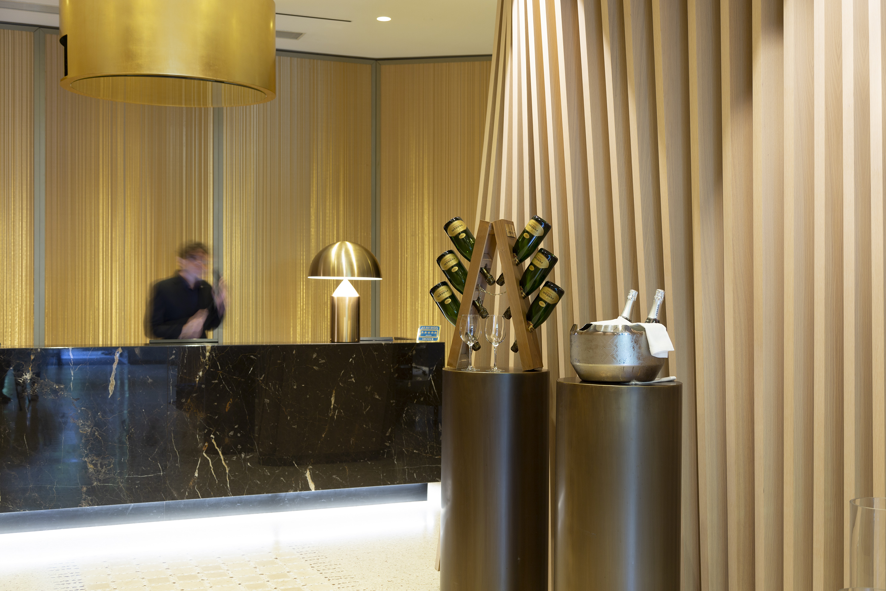 Modern hotel reception with black marble counter, gold accents, and champagne bottles.