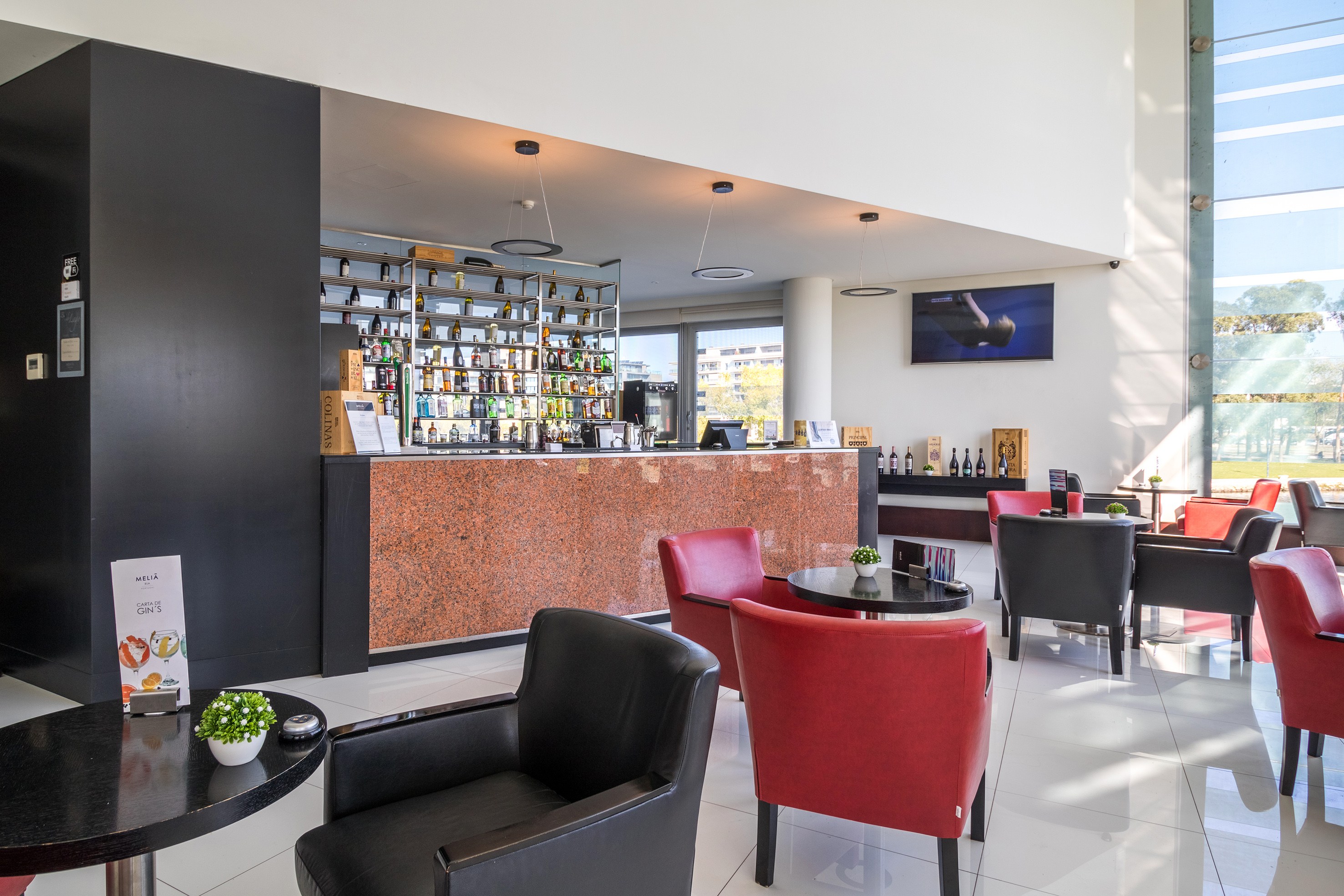 Modern hotel bar and lounge with liquor shelf, granite counter, red & black armchairs.