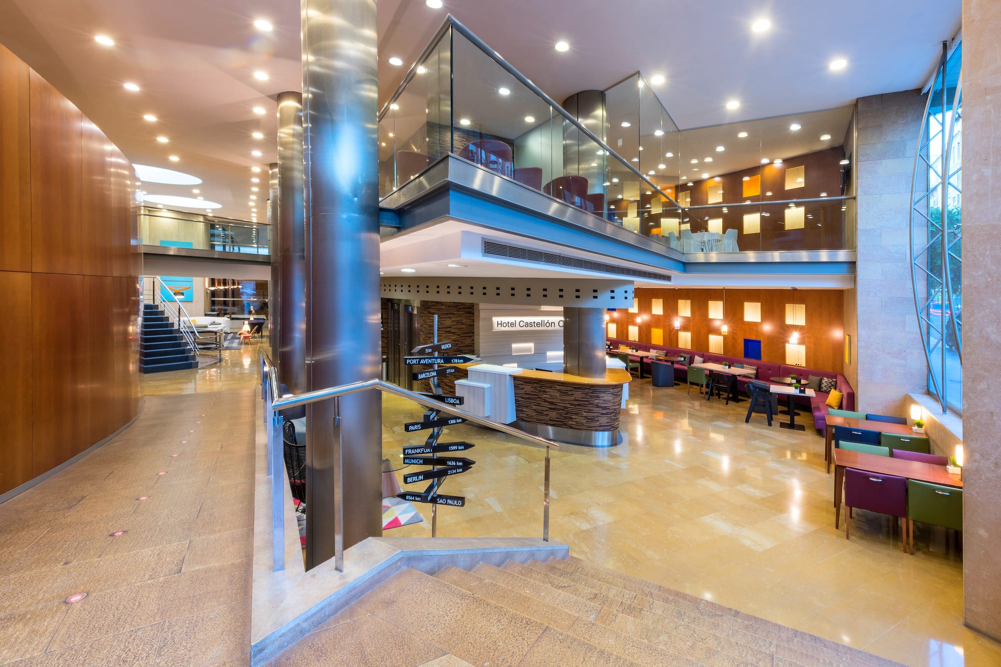 Hotel Castellón lobby with reception desk, modern lounge, and multi-city direction sign.