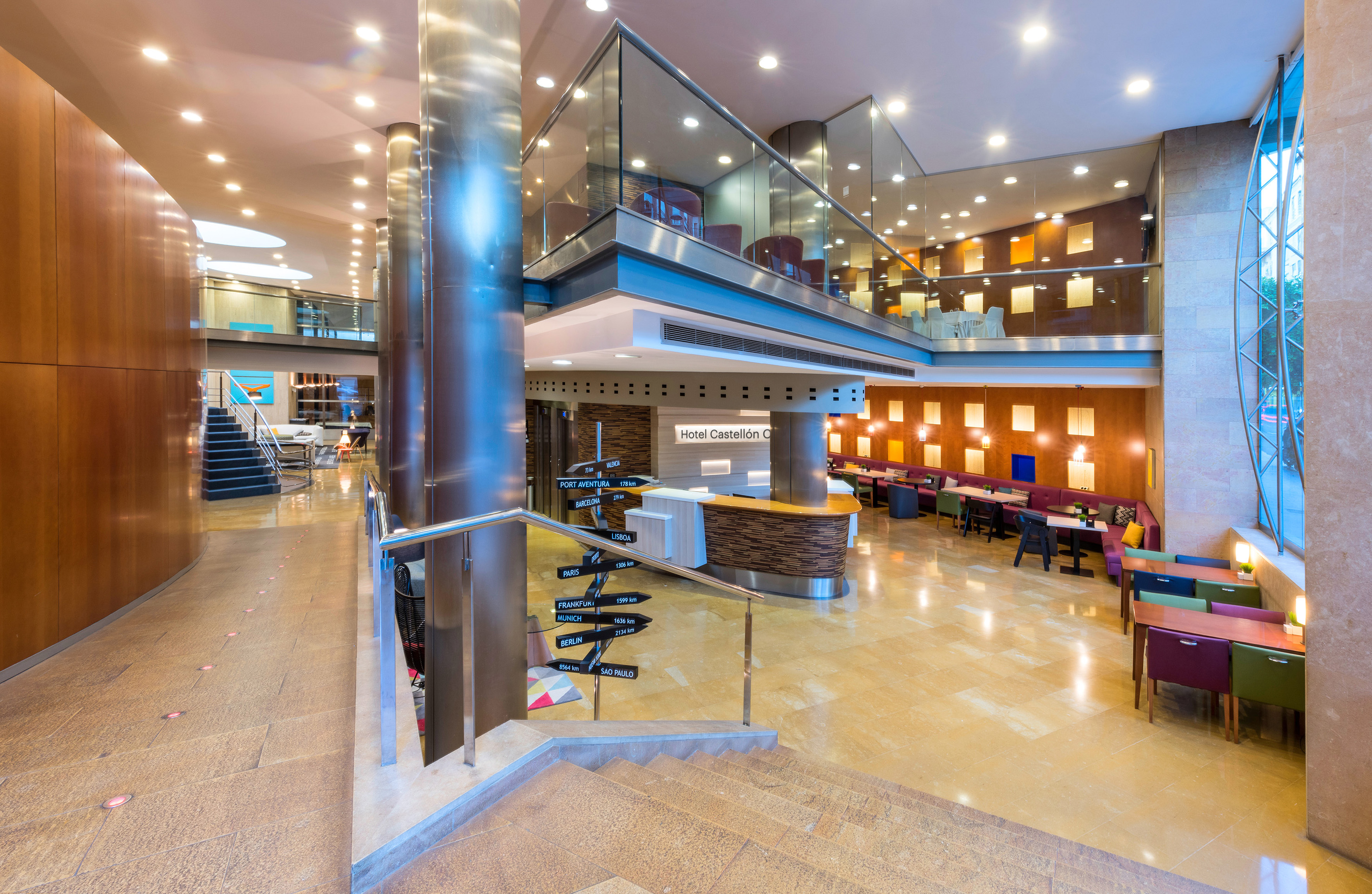 Hotel Castellón lobby with reception desk, modern lounge, and multi-city direction sign.