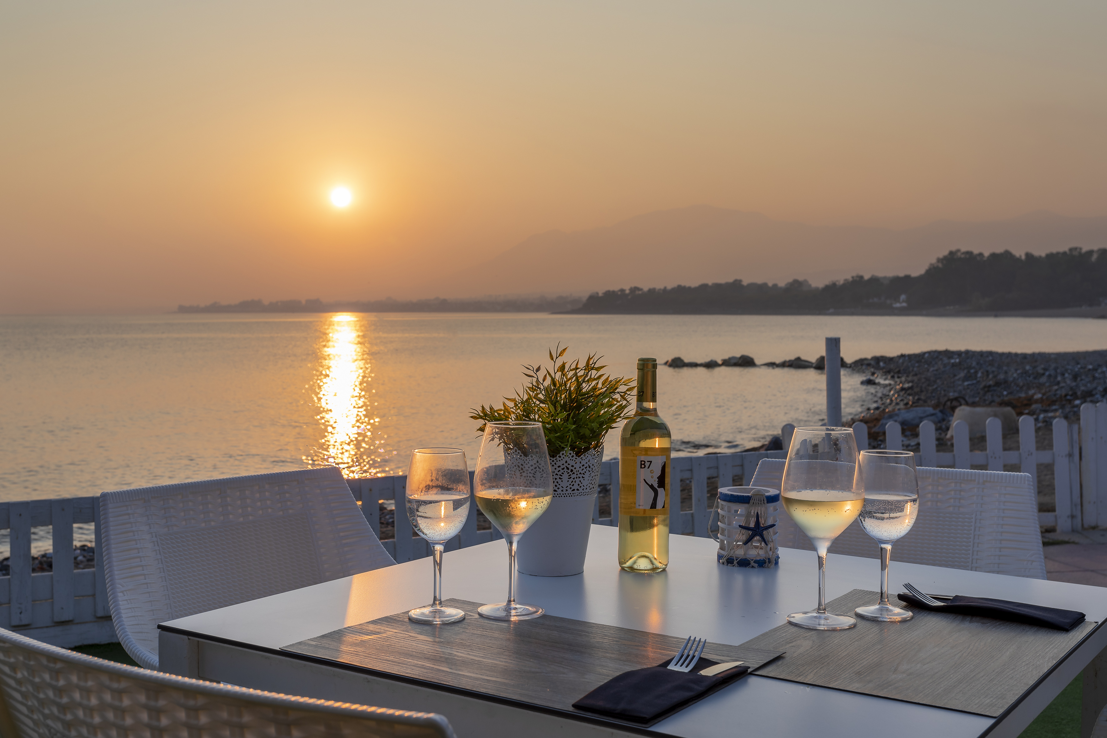 Seaside dining table with wine glasses and golden sunset ocean view.