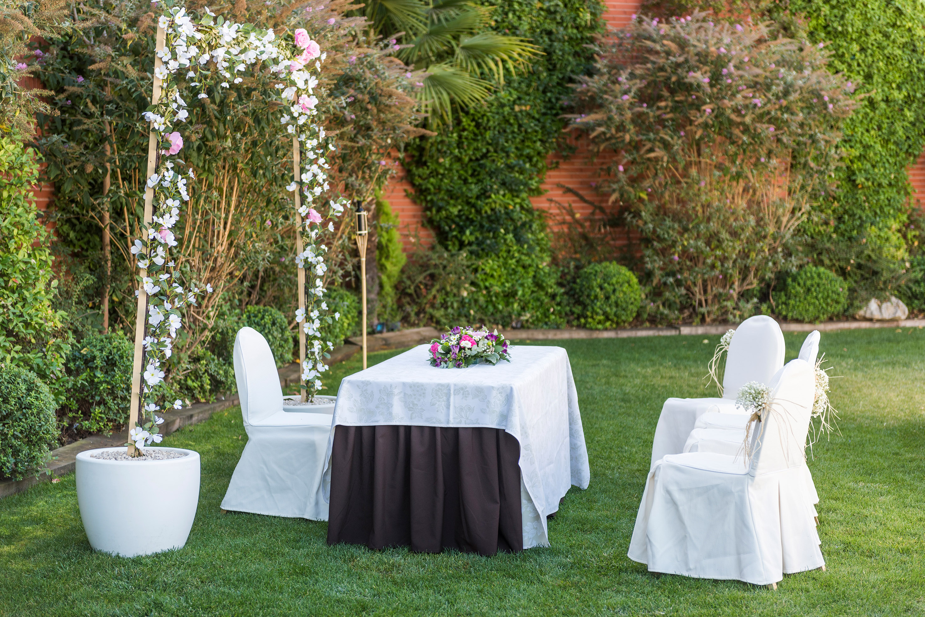 Garden wedding reception with floral arch, white chairs, and elegant table.