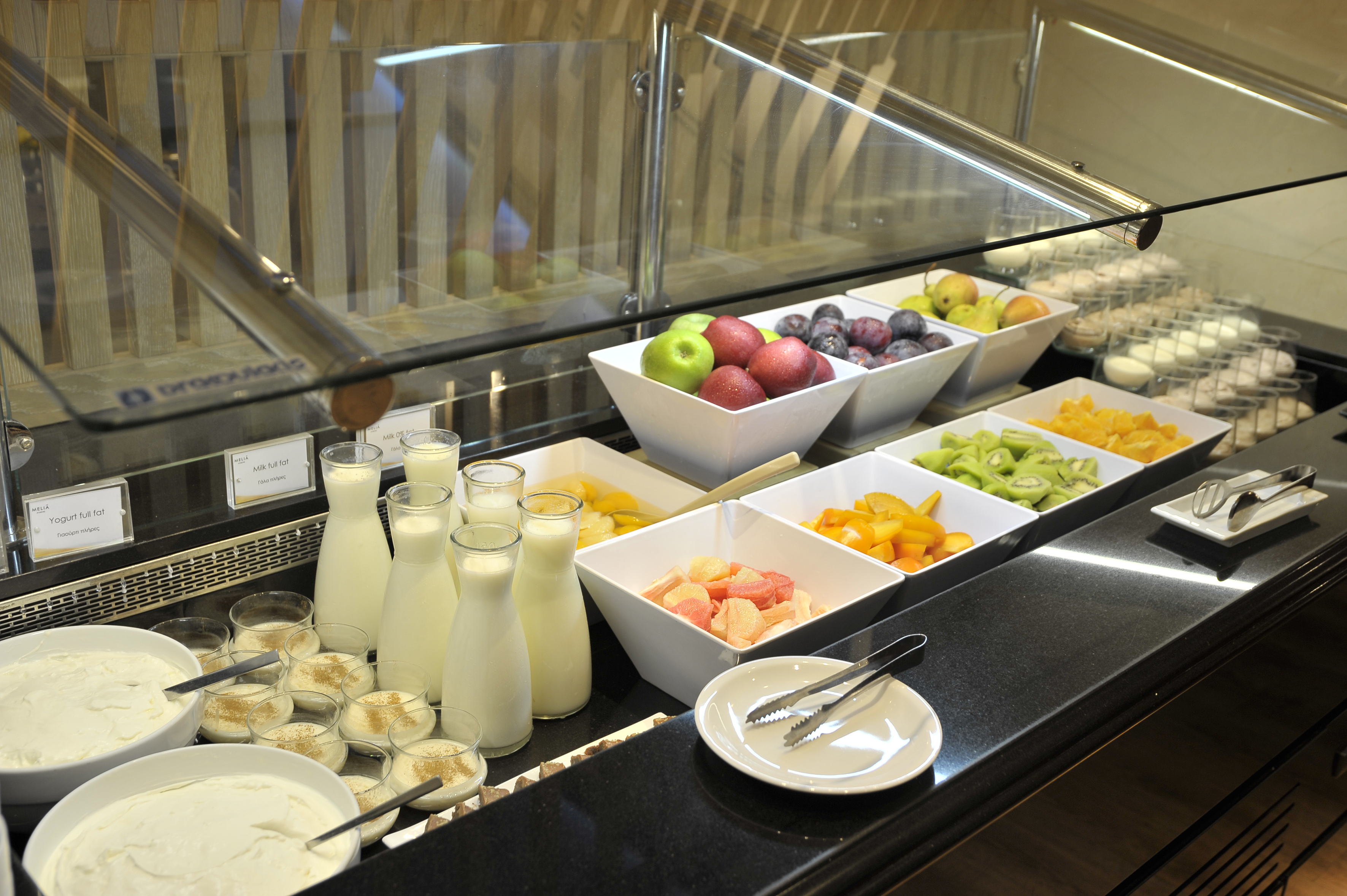 Healthy breakfast buffet with fresh fruit, yogurt, and milk on a black counter.