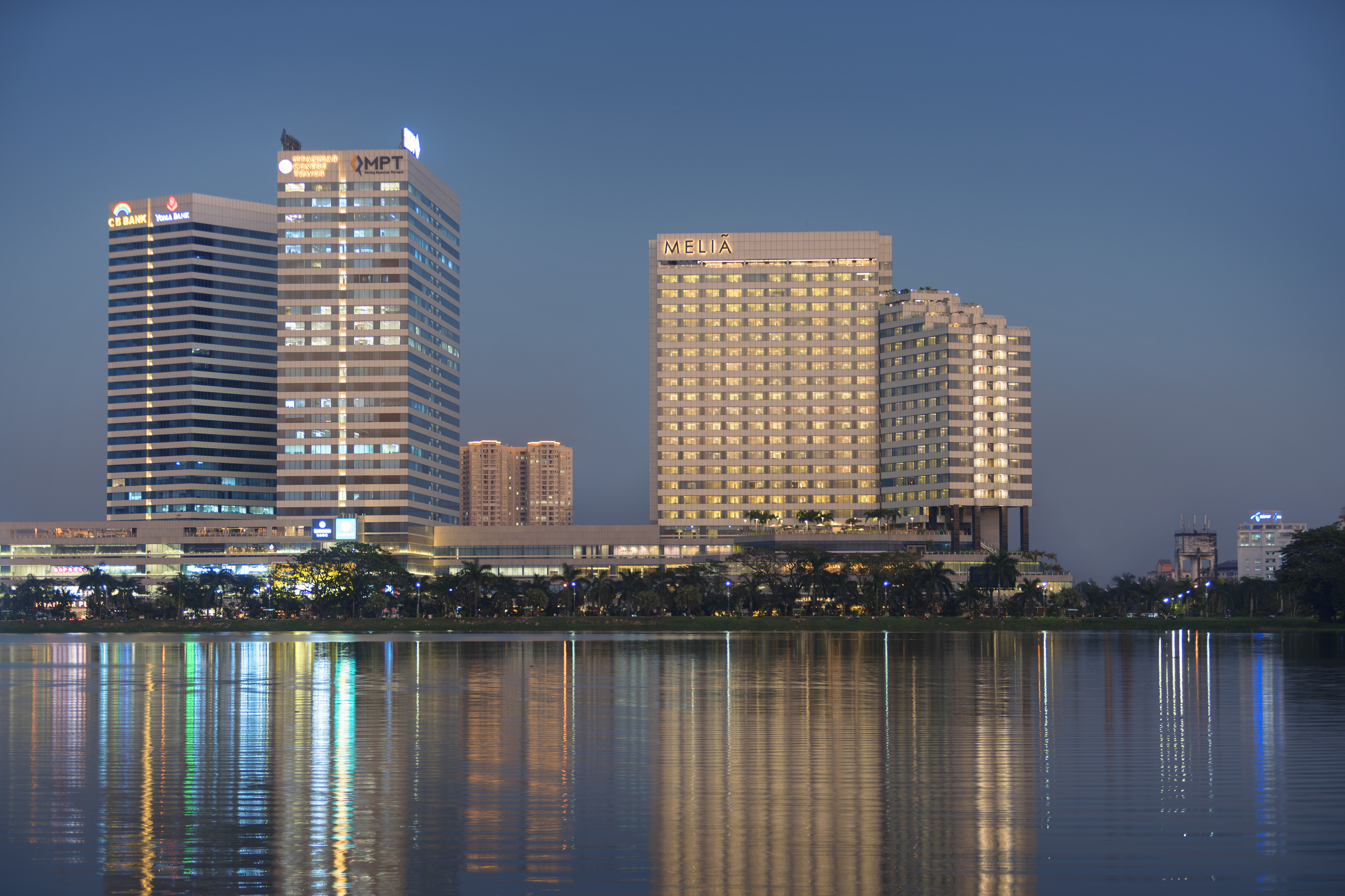 Illuminated Meliã hotel and bank skyscrapers reflecting in a city lake at night.