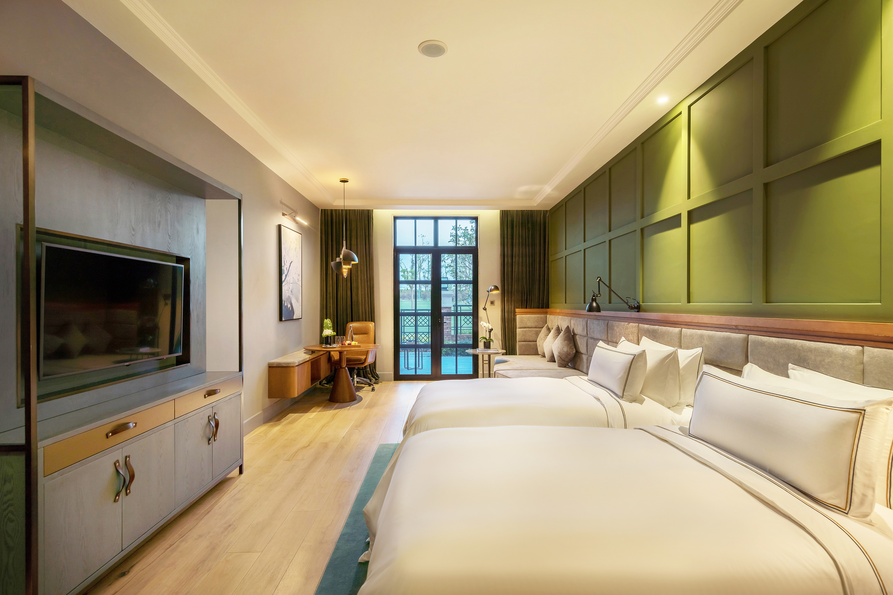 Spacious hotel room with twin beds, green paneled accent wall, and desk area.