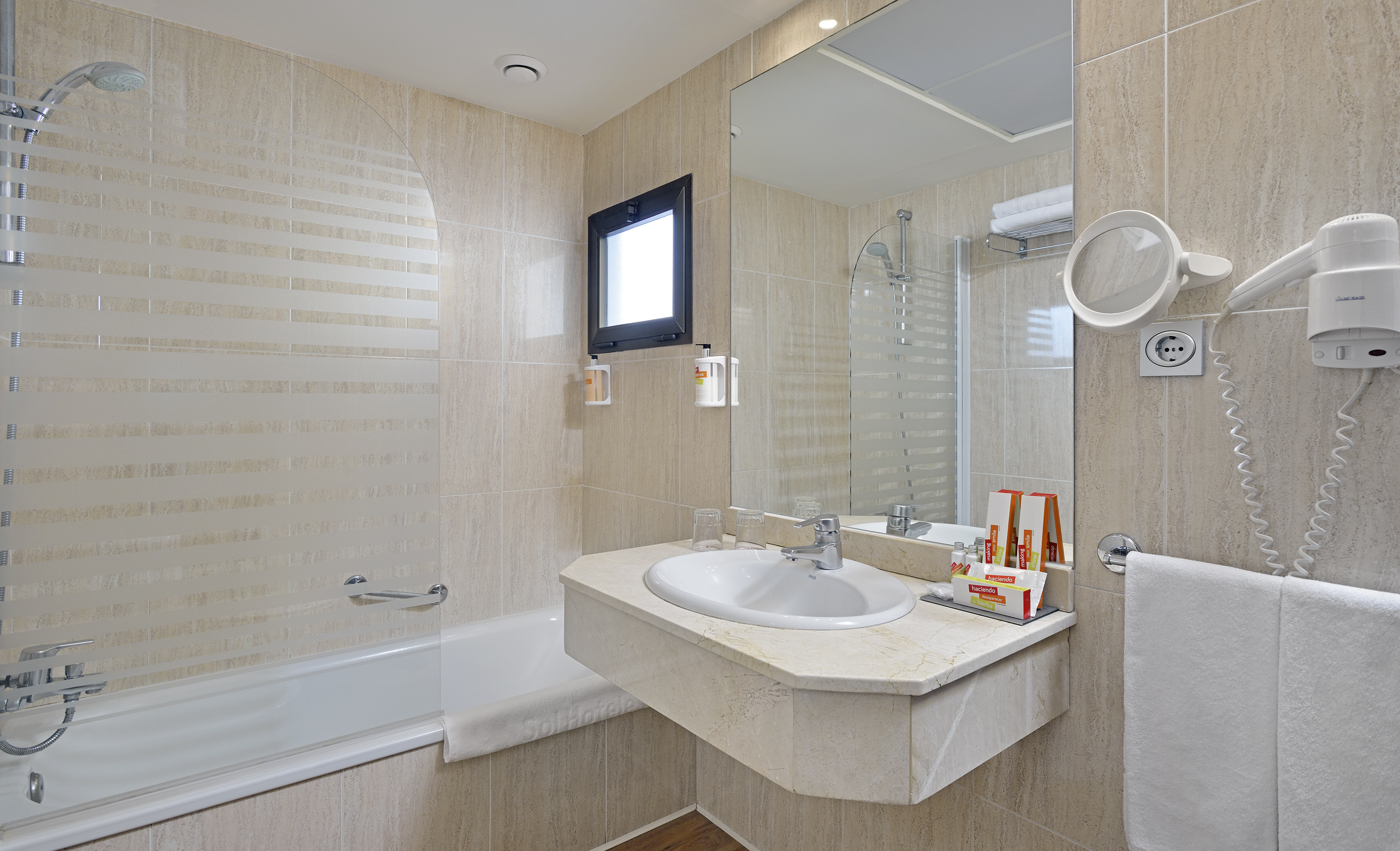 Tiled hotel bathroom with bathtub, shower, vanity sink, and mirror.